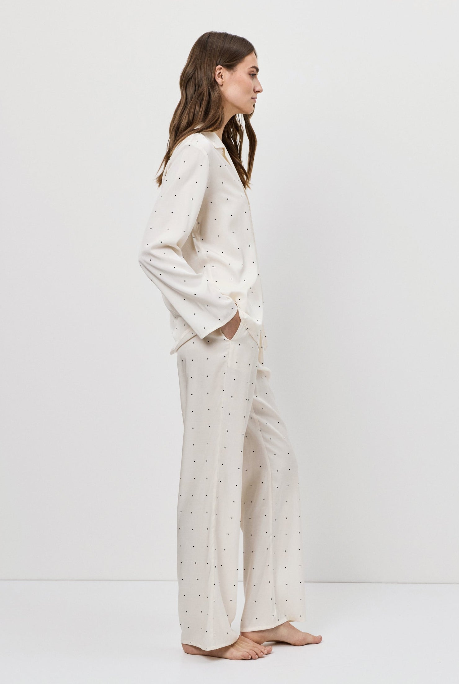 Woman wearing a white pajama set with a polka dot pattern on a plain background