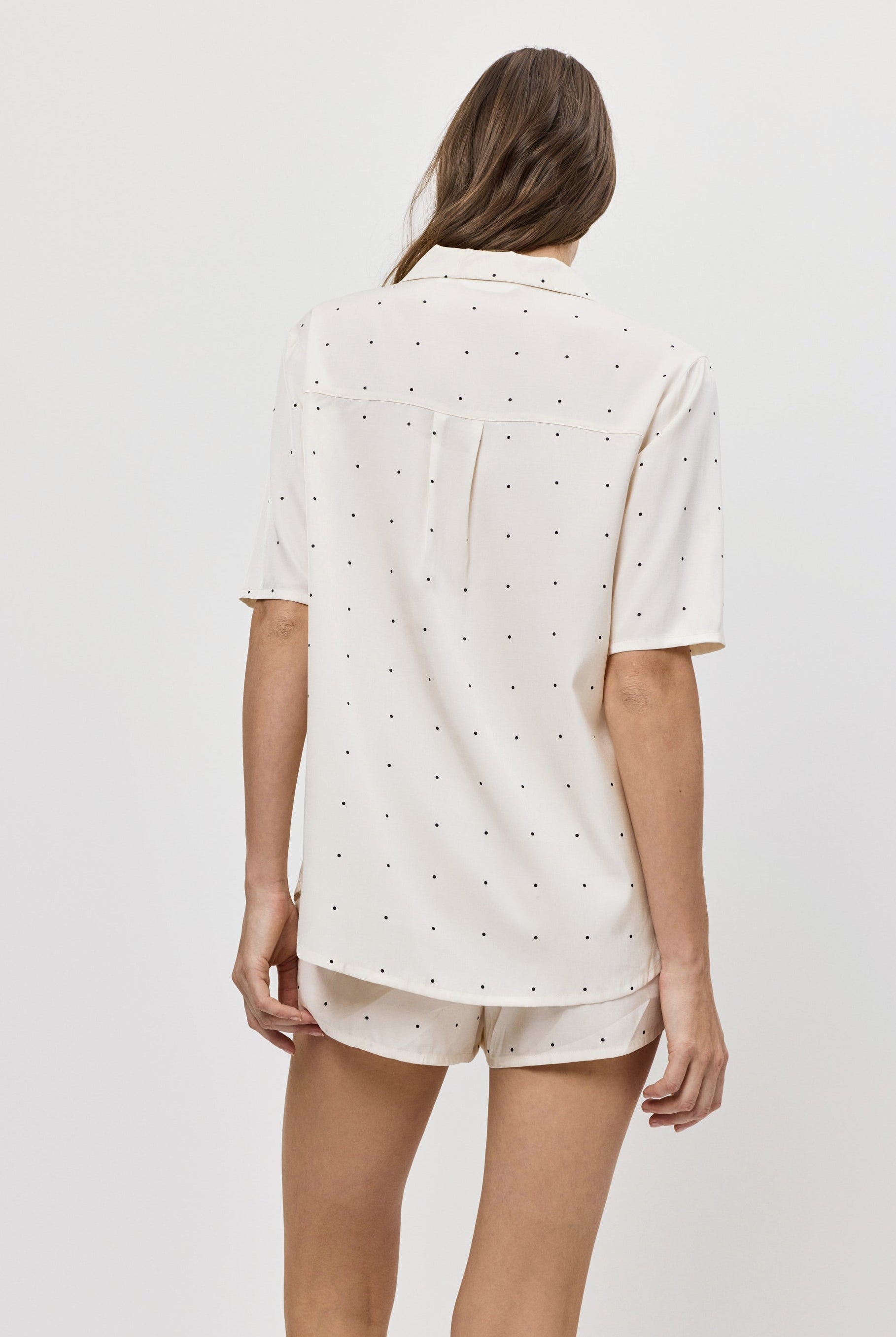 Woman wearing a white polka dot pajama set with shorts on a plain background