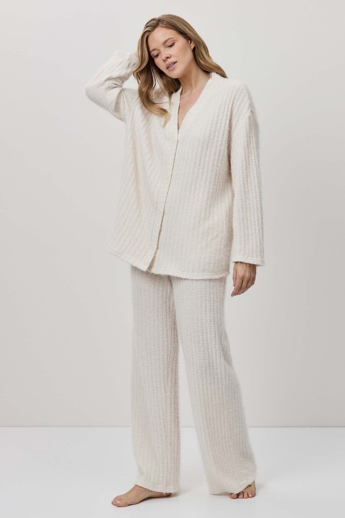 Woman wearing a white ribbed pajama set against a white background