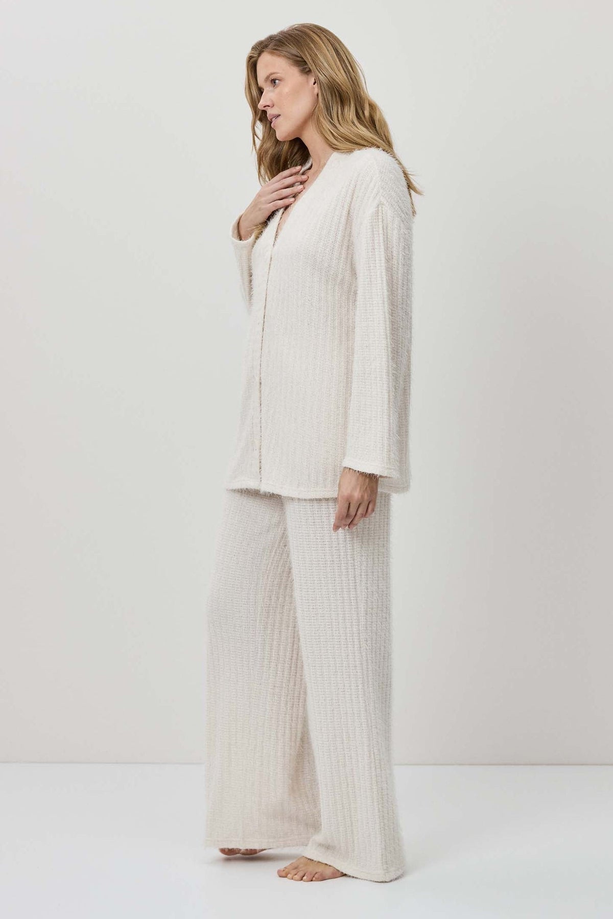 Woman wearing a white outfit with wide-leg pants against a plain background