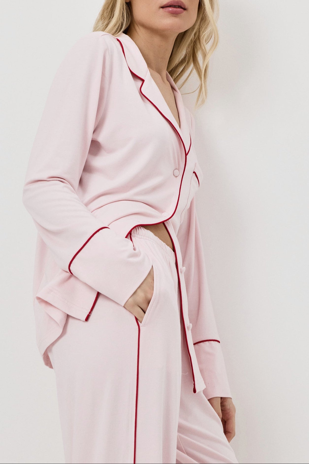 Woman wearing a pink pajama set with red piping on a white background
