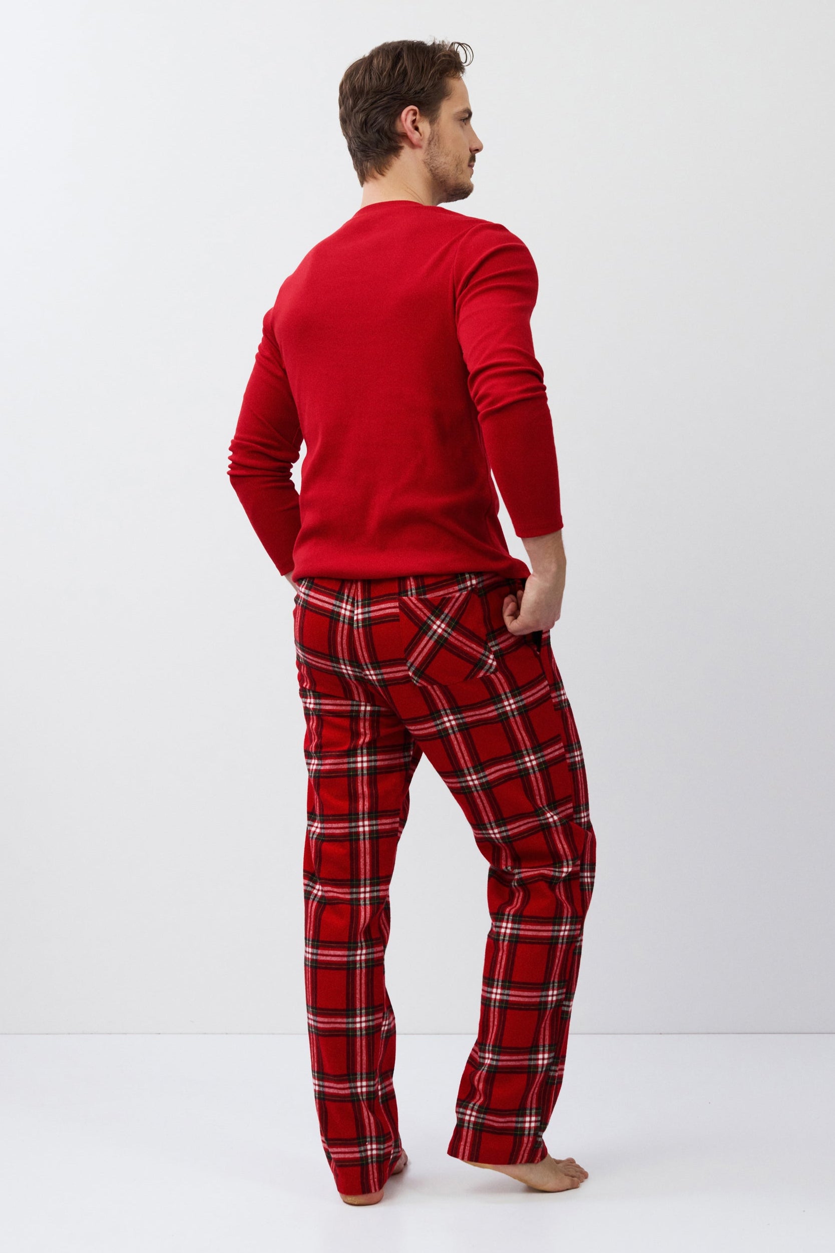 Man wearing red plaid pajama pants and a matching shirt on a white background