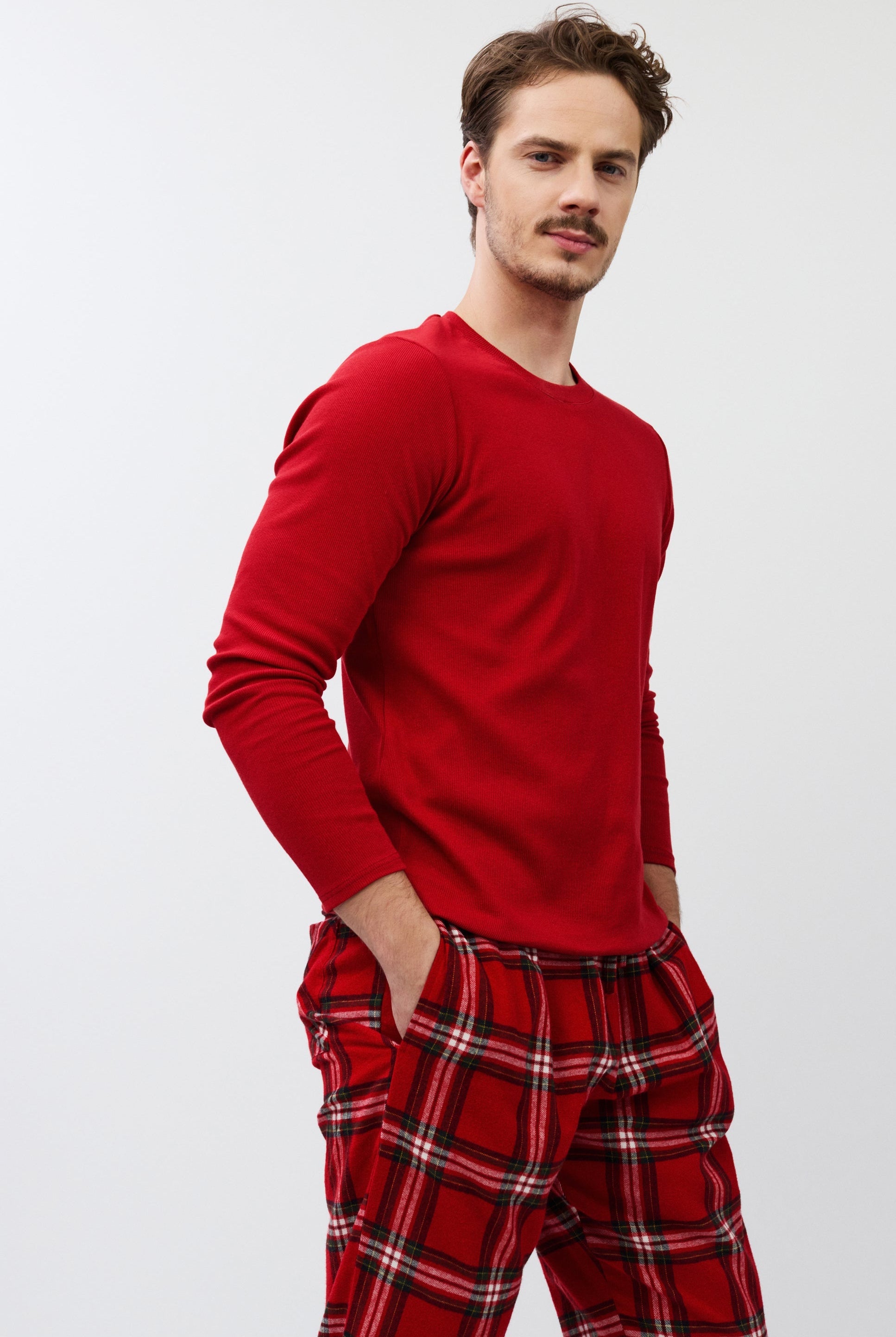 Man wearing a red long-sleeve shirt and plaid pants on a white background