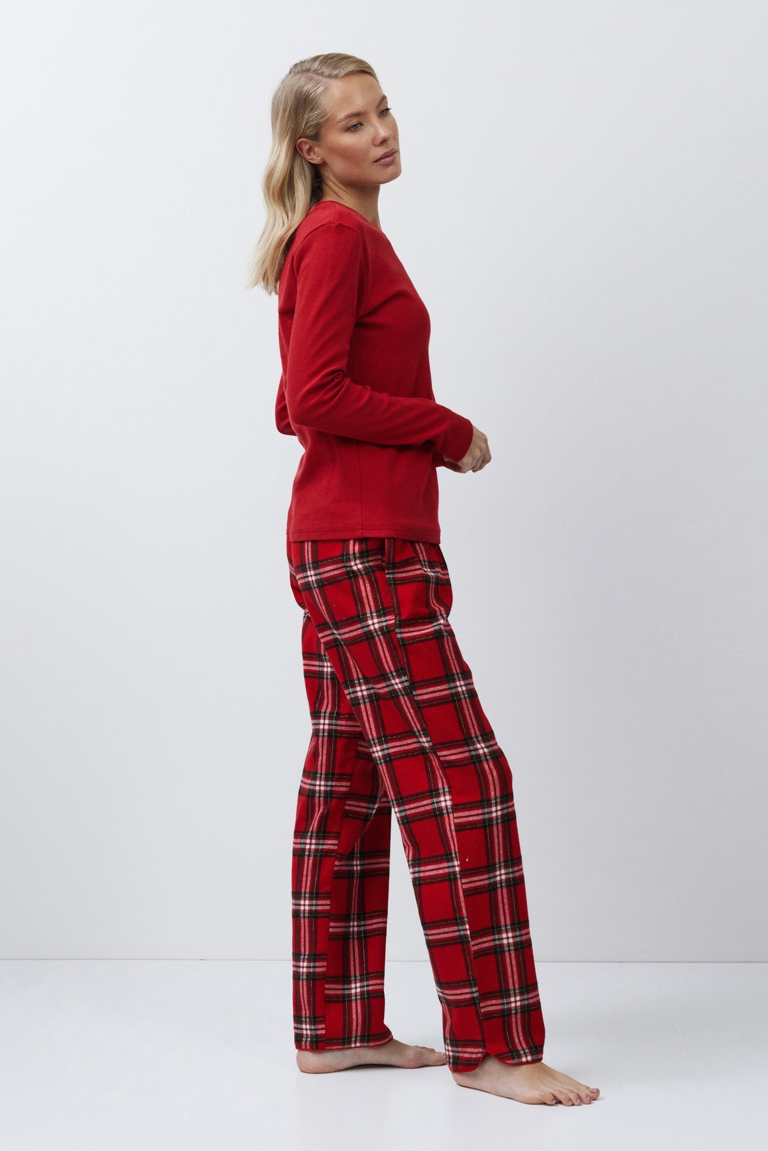 Person wearing red pajama top and plaid pants on a white background