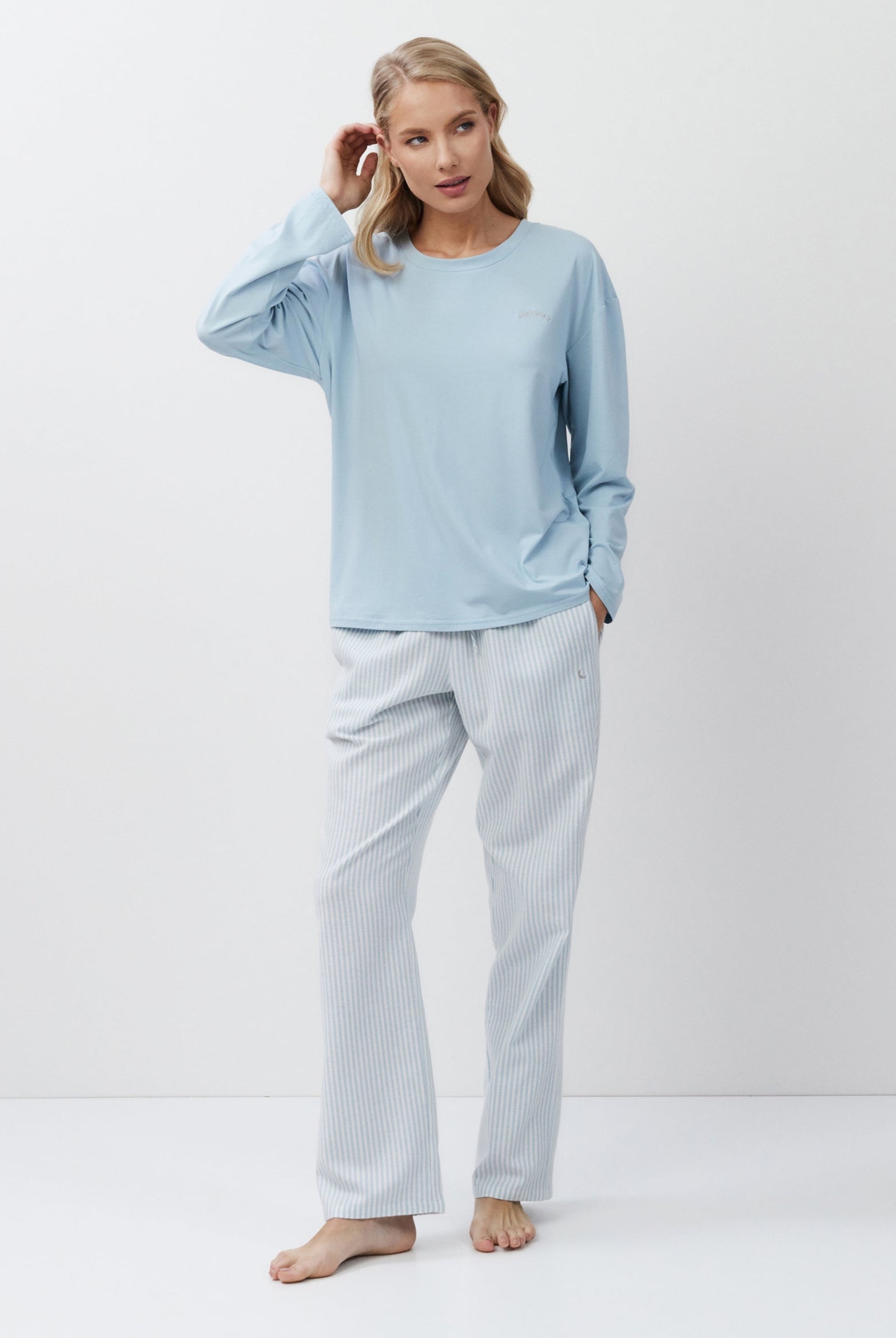 Woman wearing light blue pajama top and pants on a white background