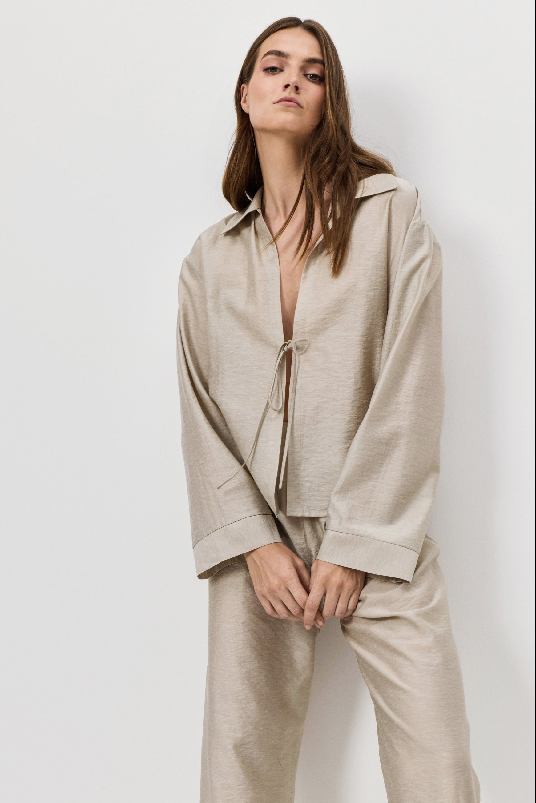 Woman wearing a beige shirt and pants against a white background