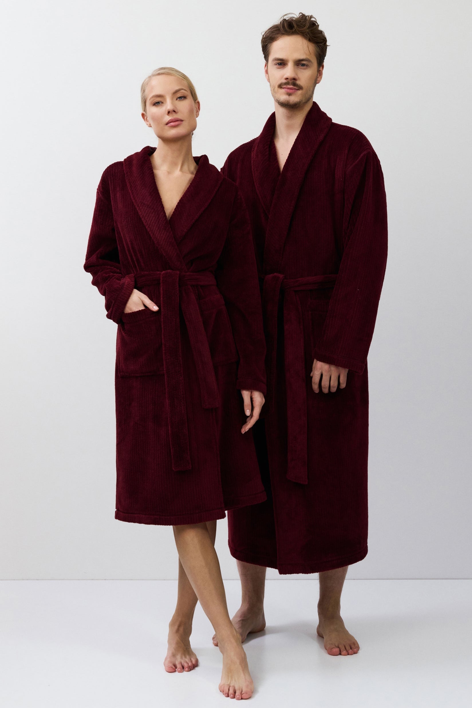 Two people wearing burgundy robes standing side by side on a white background