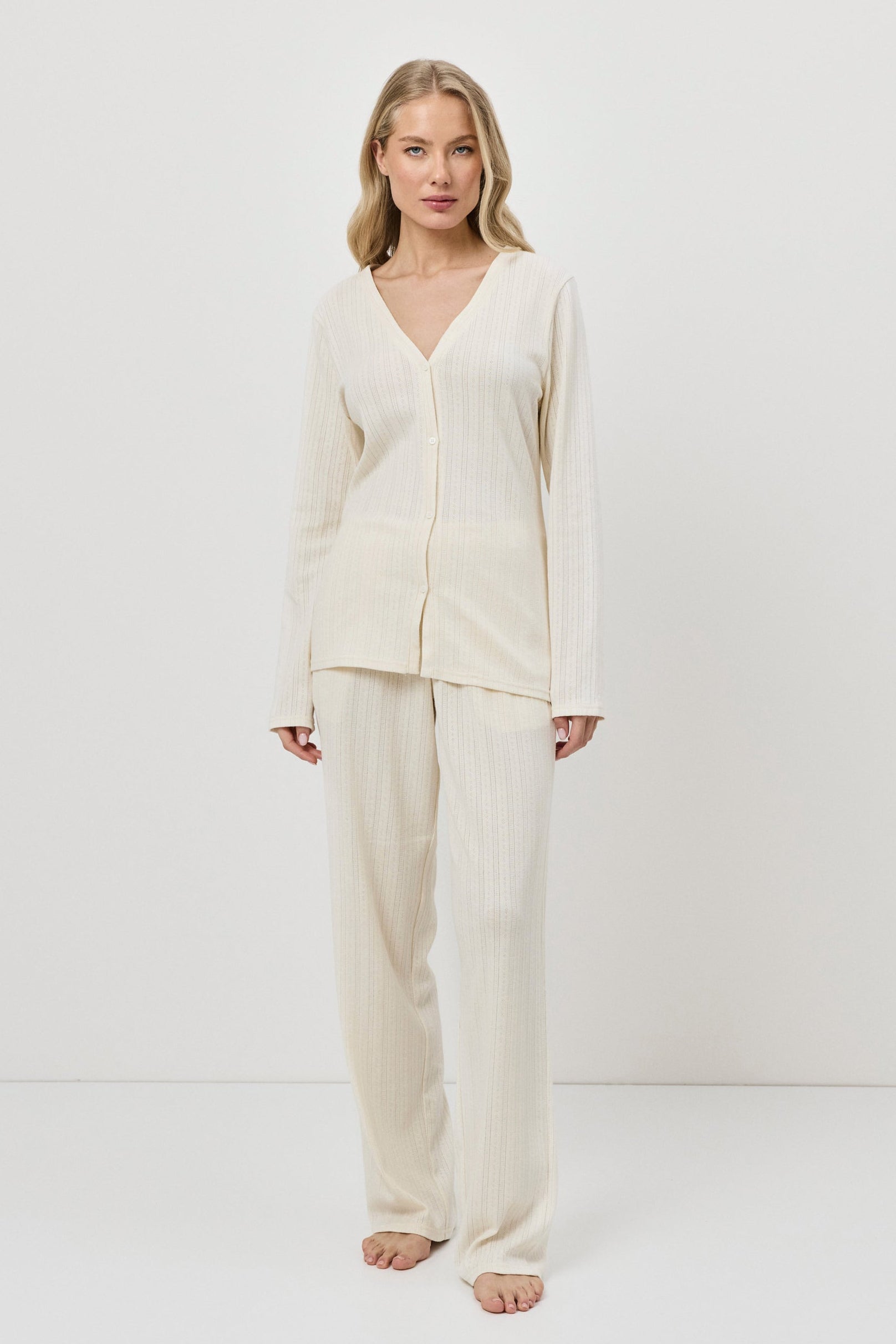 Woman wearing a cream-colored pajama set with pants against a white background