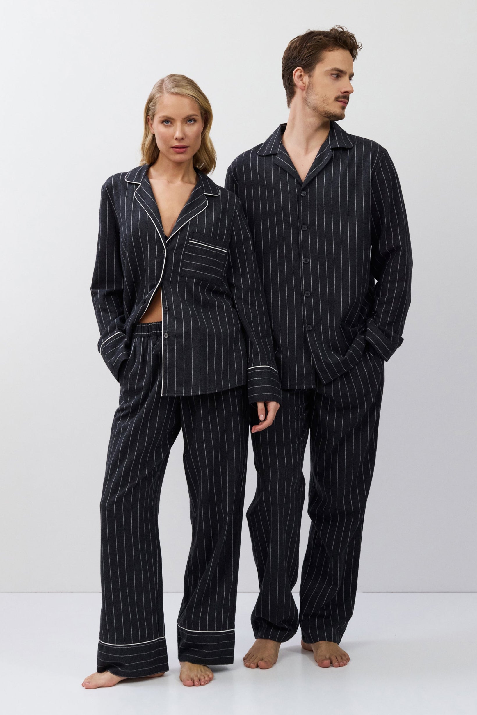 Two people wearing matching gray pinstripe pajamas on a white background