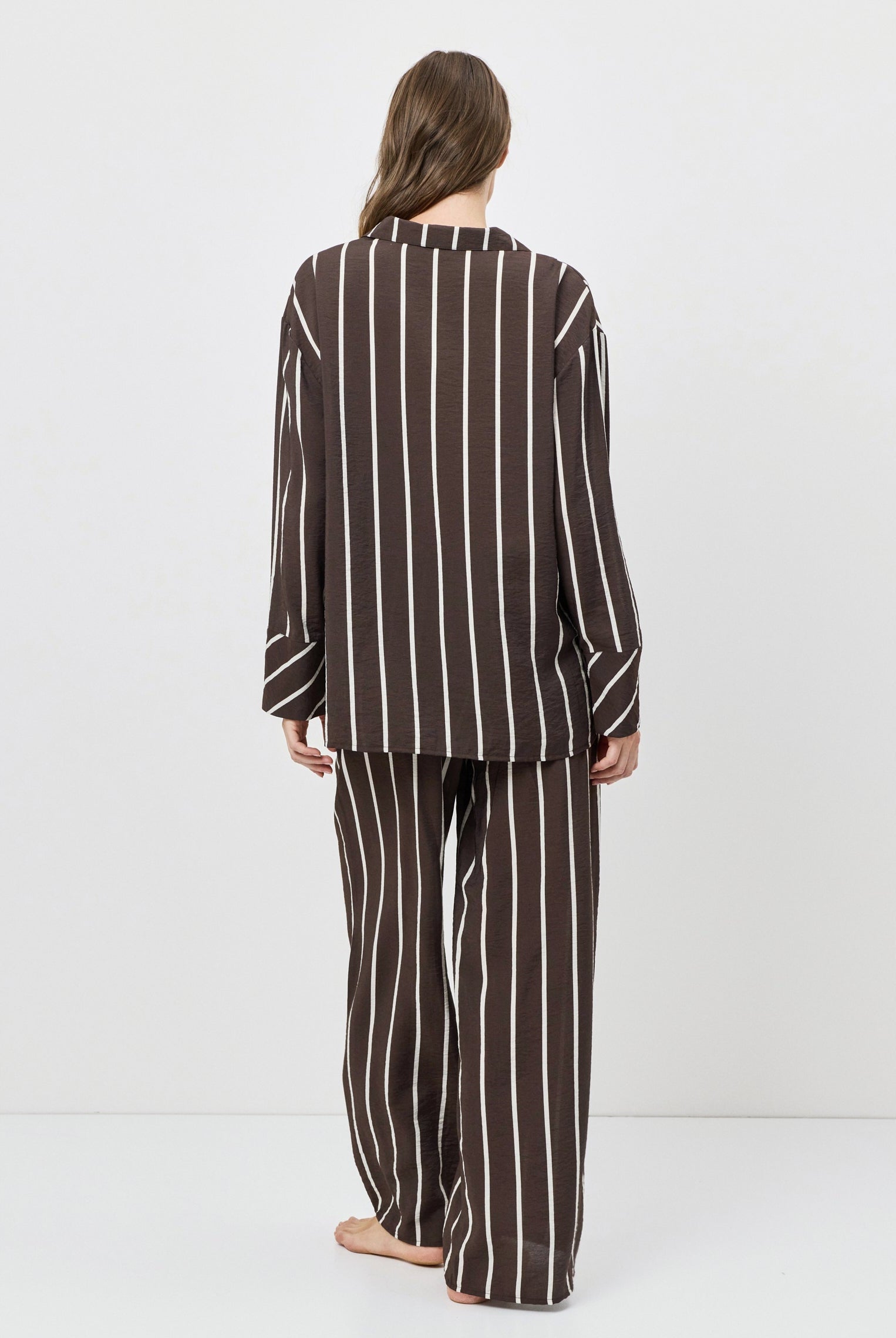 Person wearing a brown and white striped pajama set on a white background