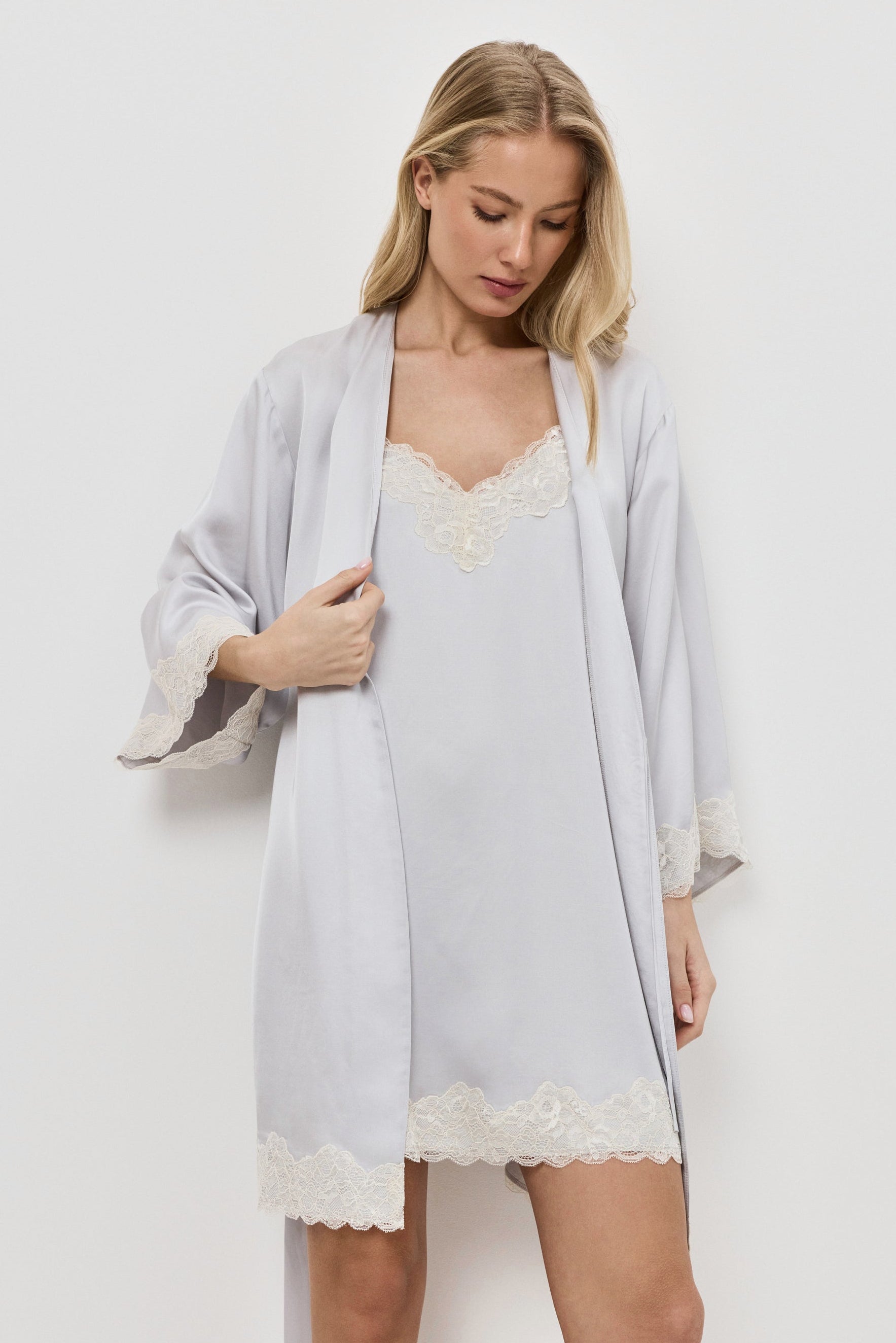 Woman wearing a light gray gown over a gray nightdress on a plain background