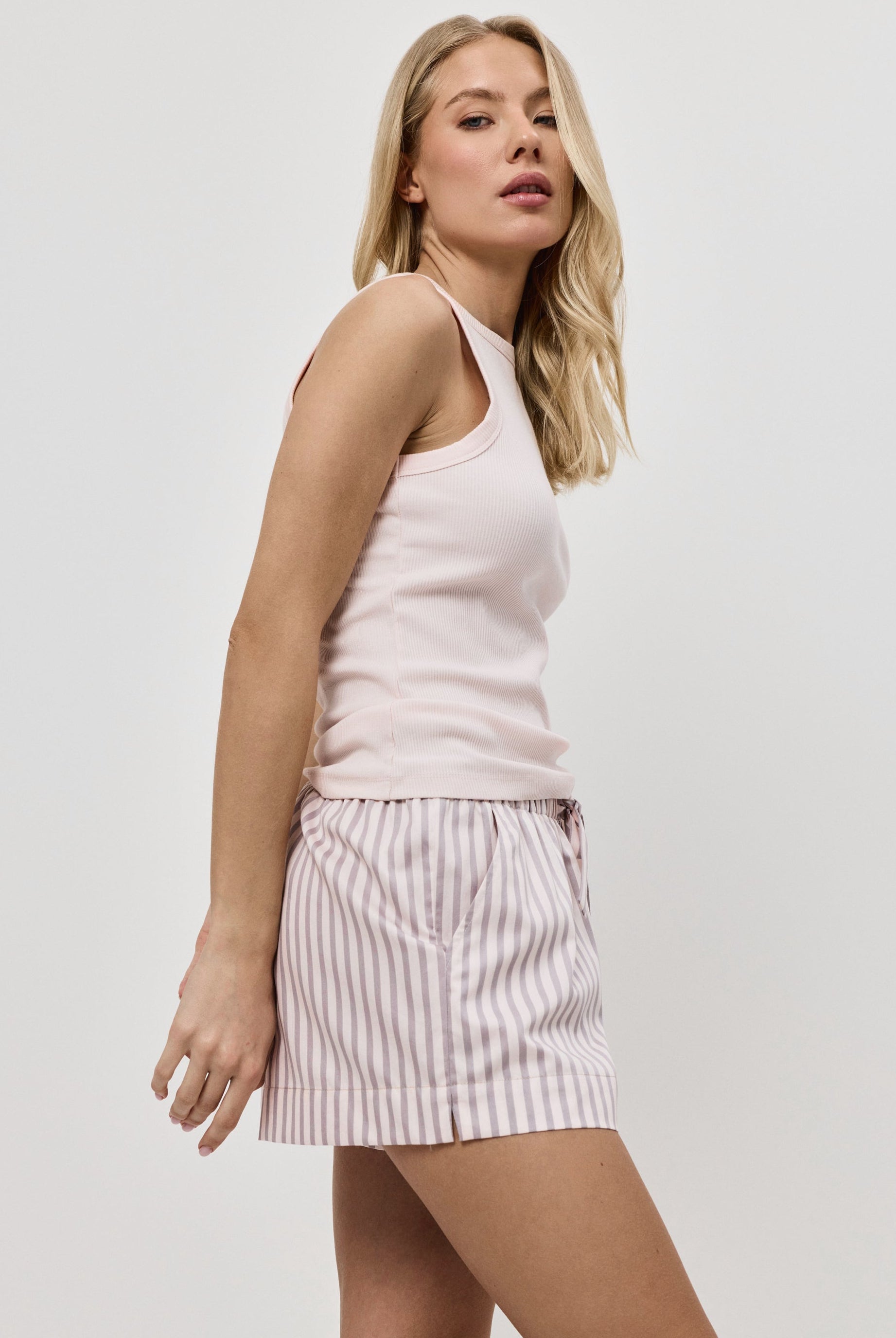 Woman wearing a light pink sleeveless top and striped pajama shorts on a white background