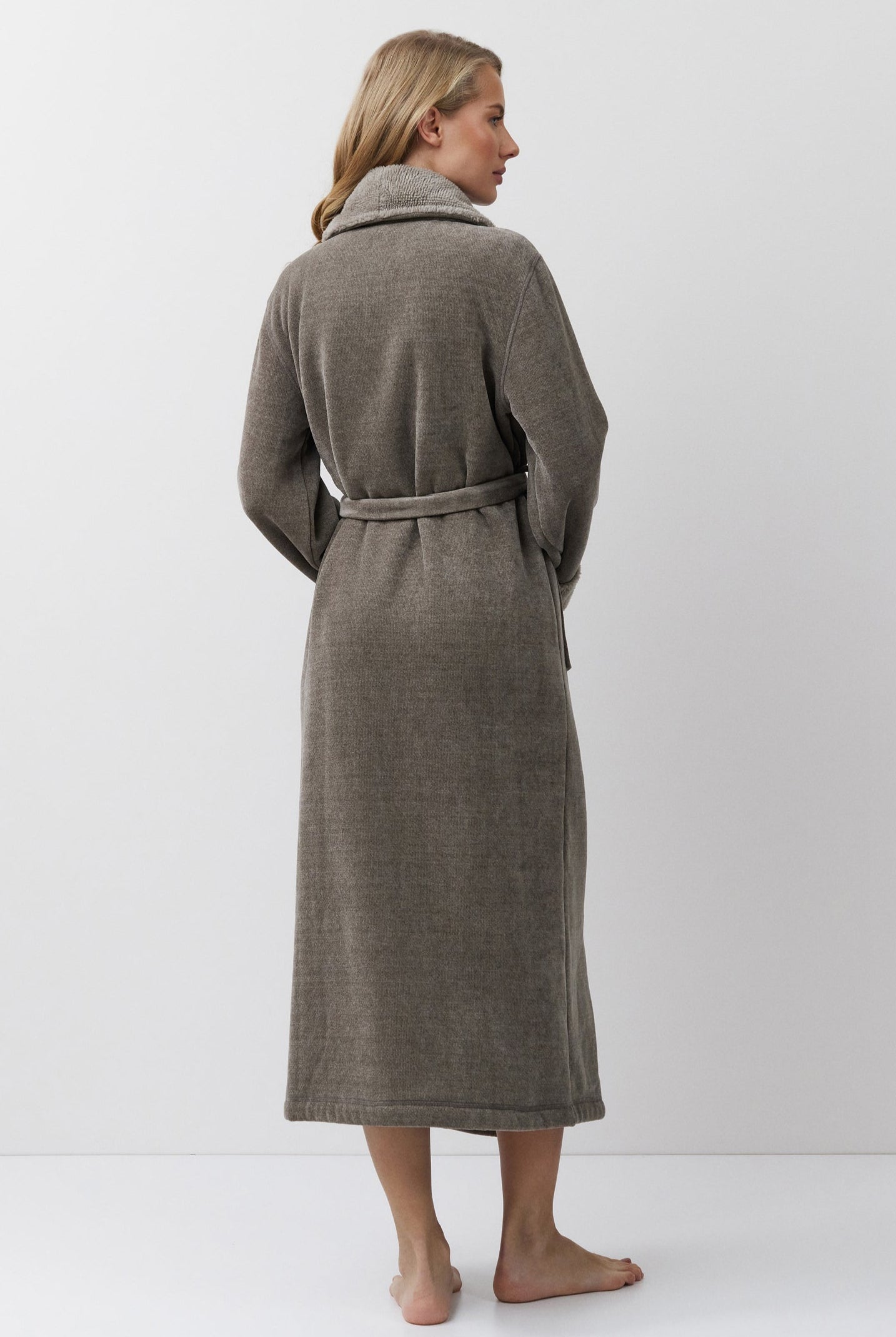 Woman wearing a brown bathrobe standing against a white background