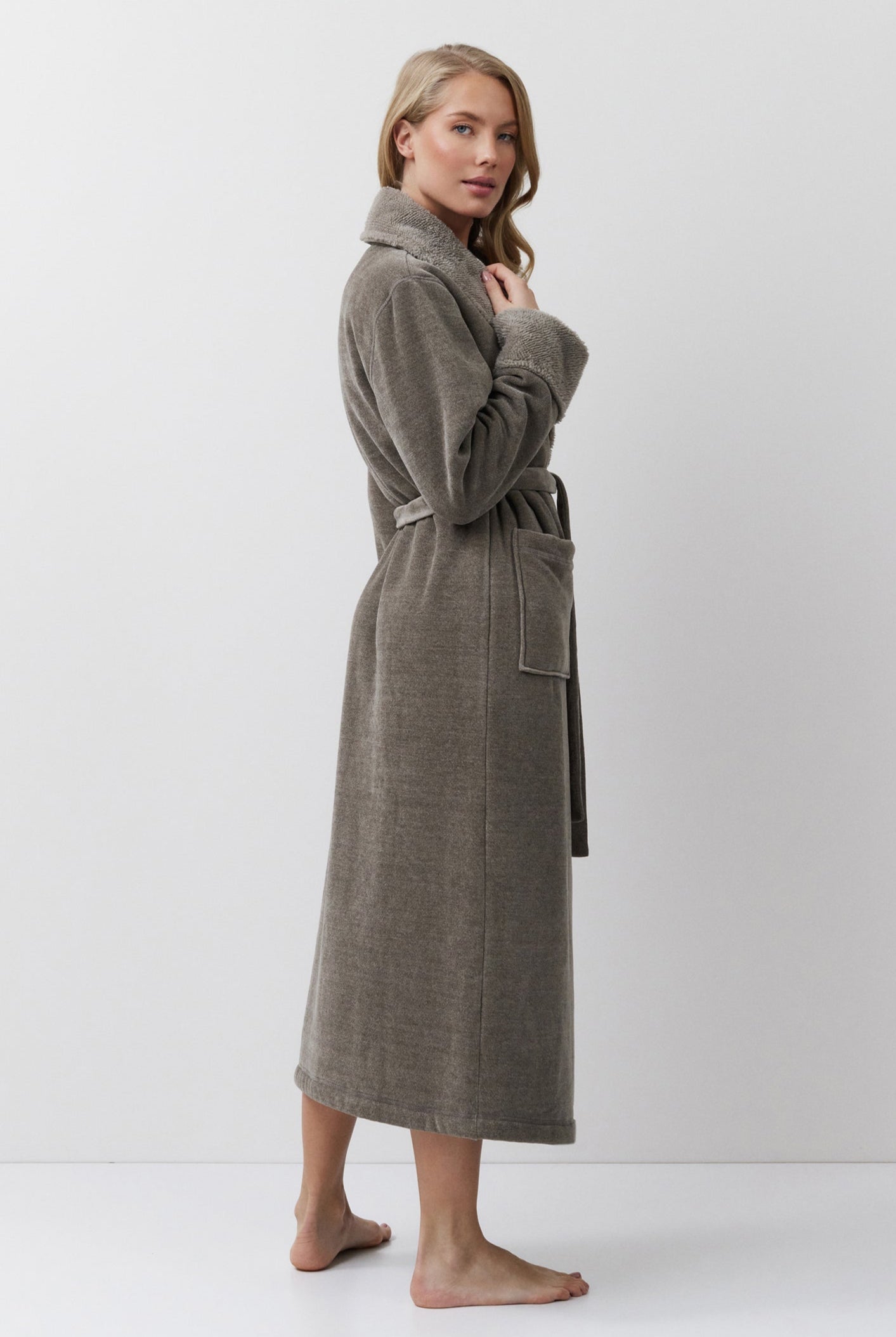 Woman wearing a brown bathrobe standing against a white background