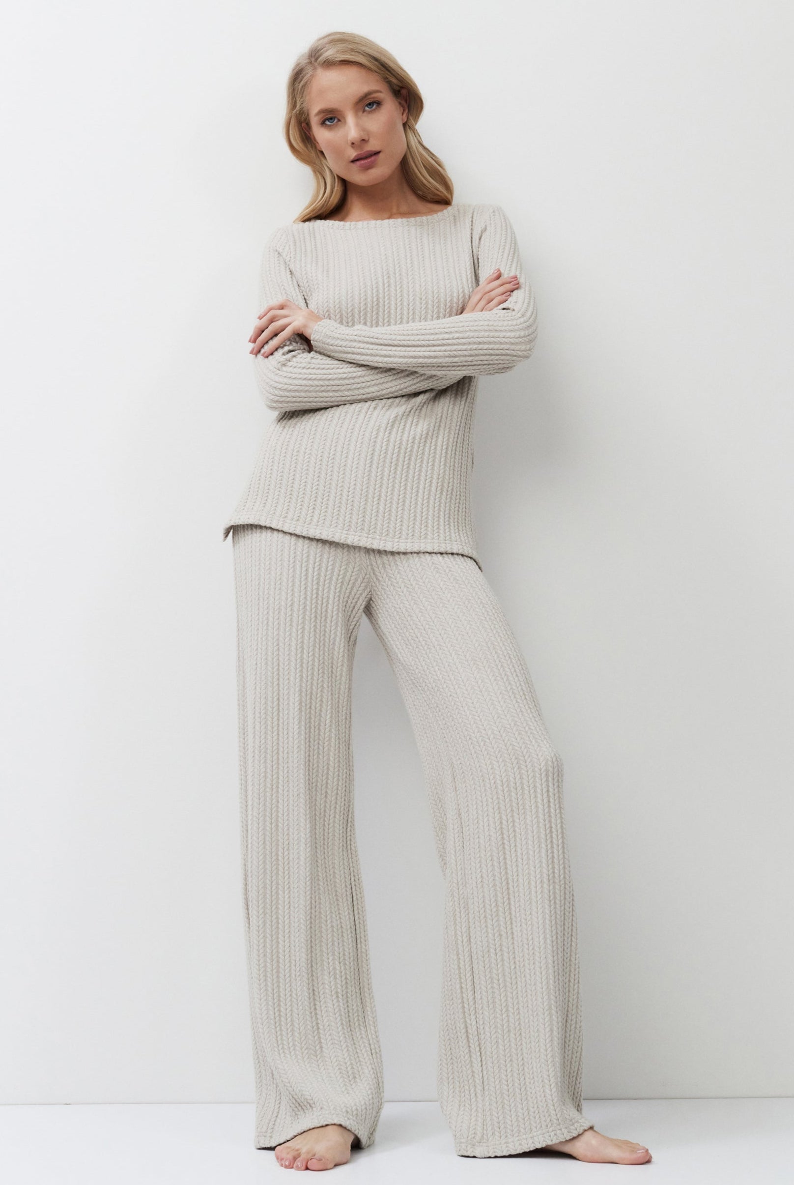 Woman wearing a beige ribbed sweater and pants against a white background