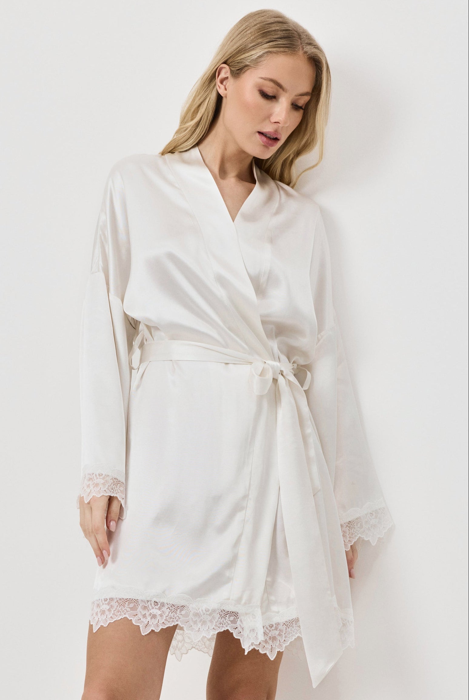 Woman wearing a white gown with lace hem on a plain background