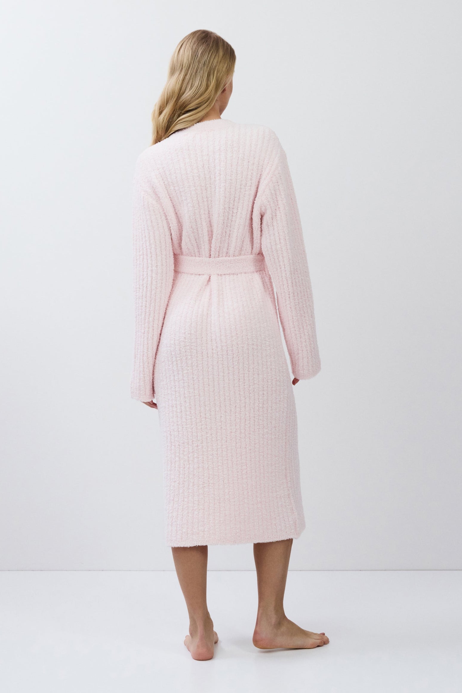 Woman wearing a light pink ribbed bathrobe against a white background