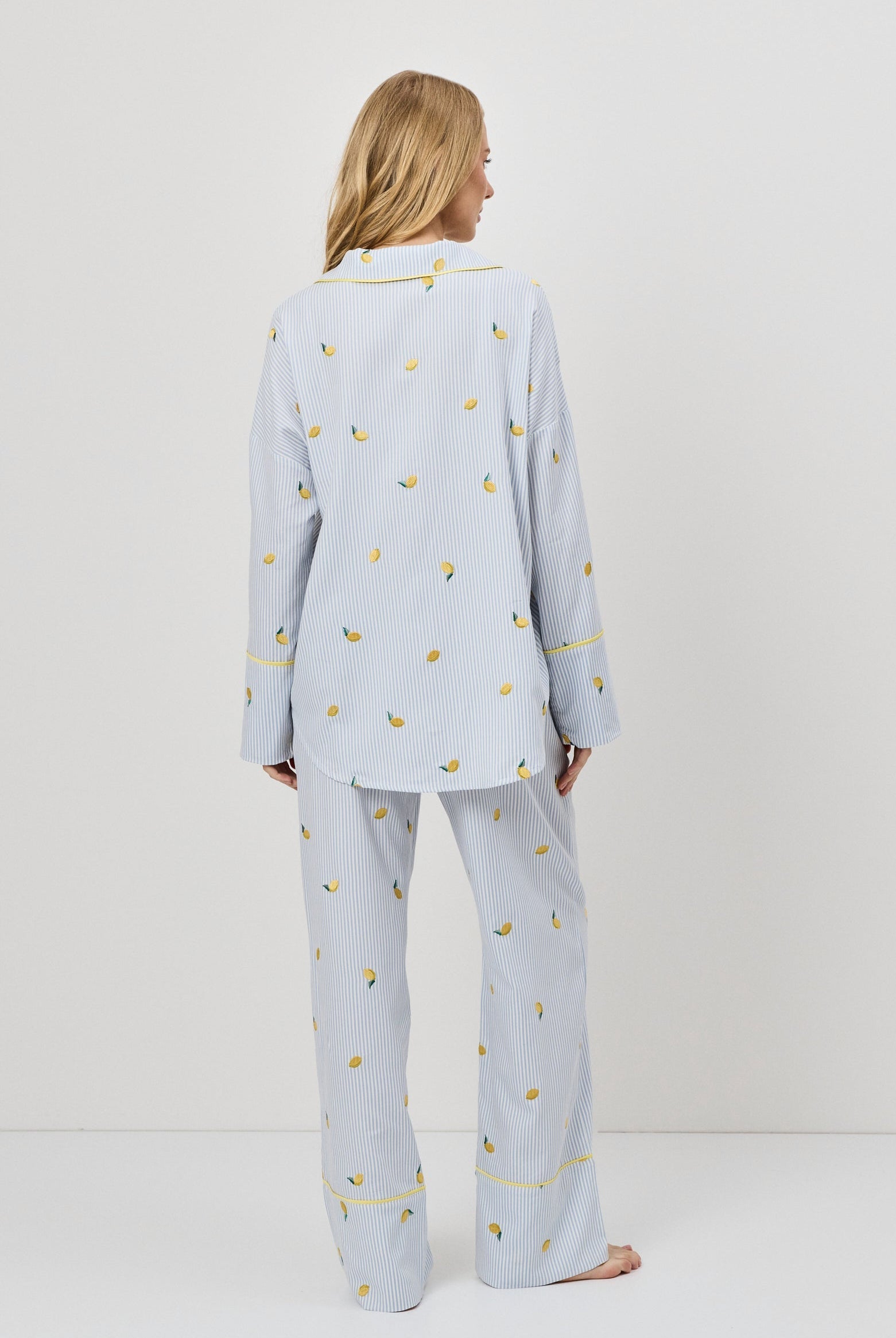 Woman wearing light blue pajama set with small lemons embroideries on a white background