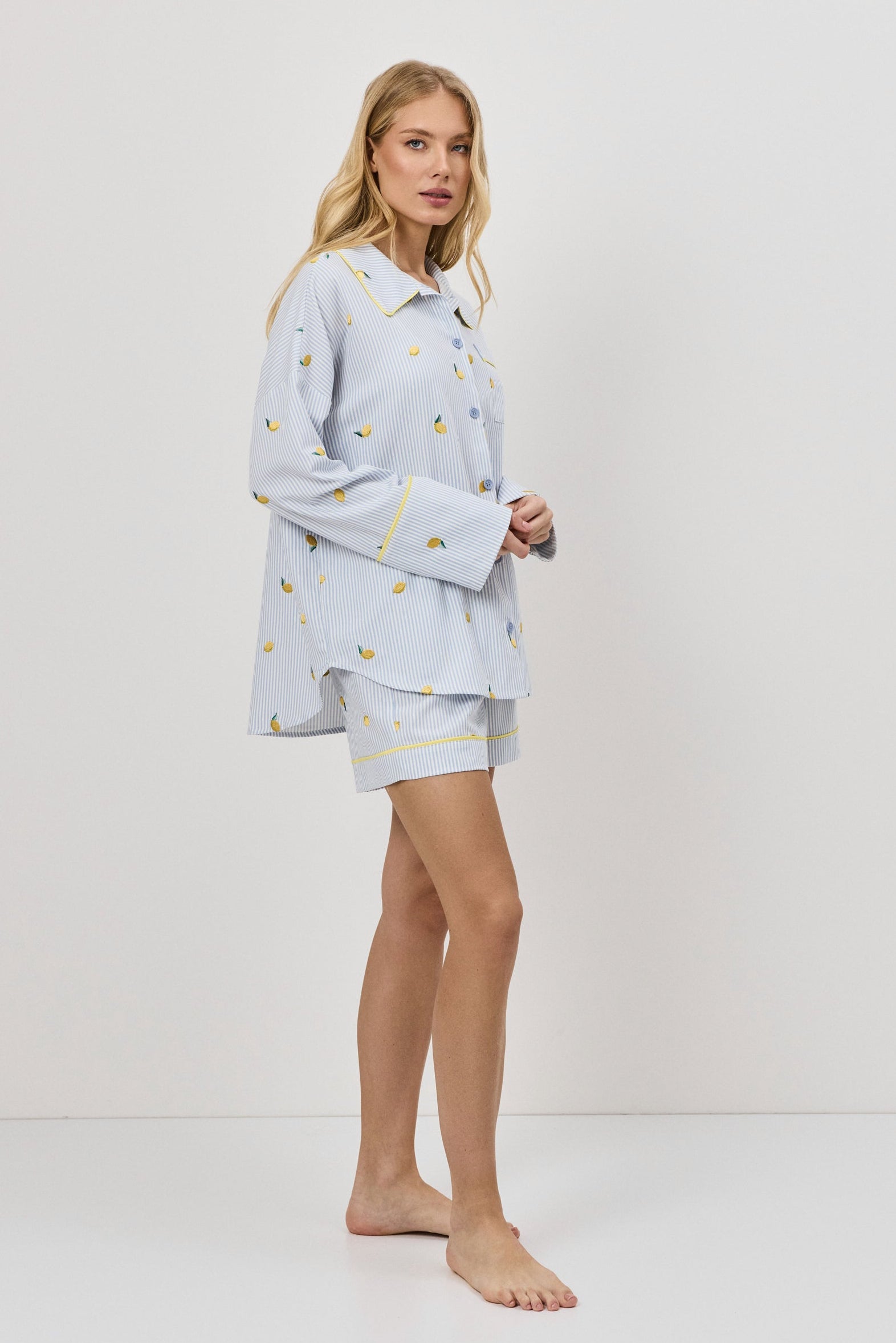 Woman wearing a light blue pajama set with lemon embroideries on a white background