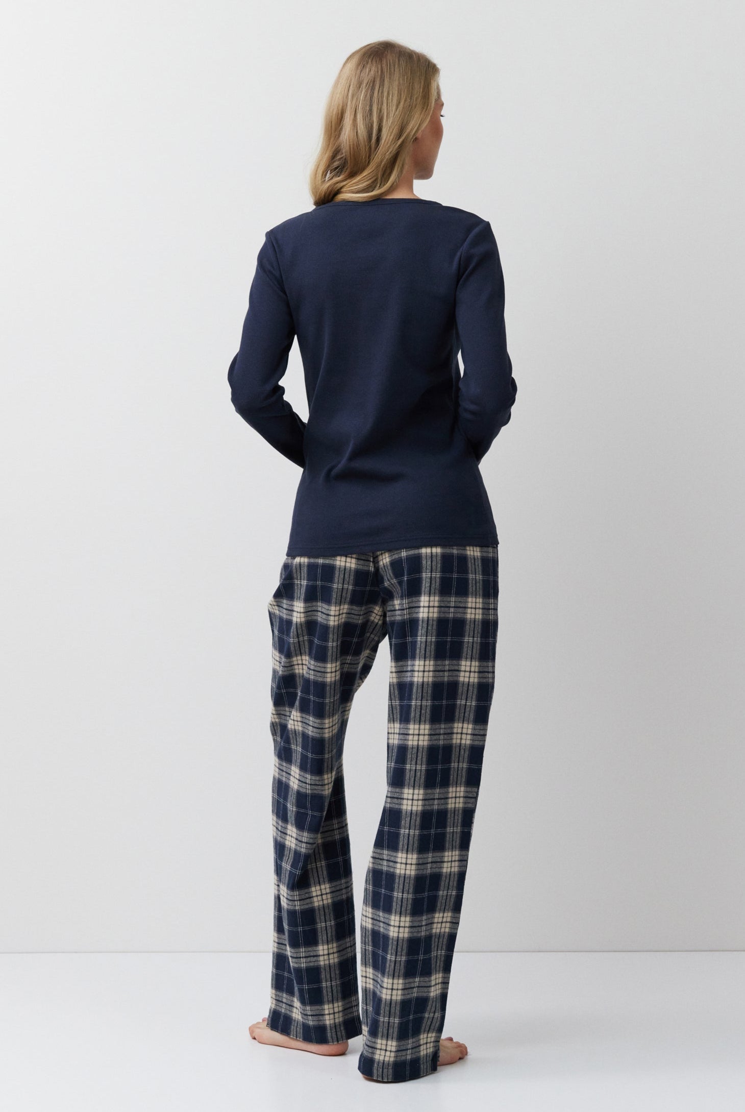 Person wearing a navy long-sleeve top and plaid pants on a white background