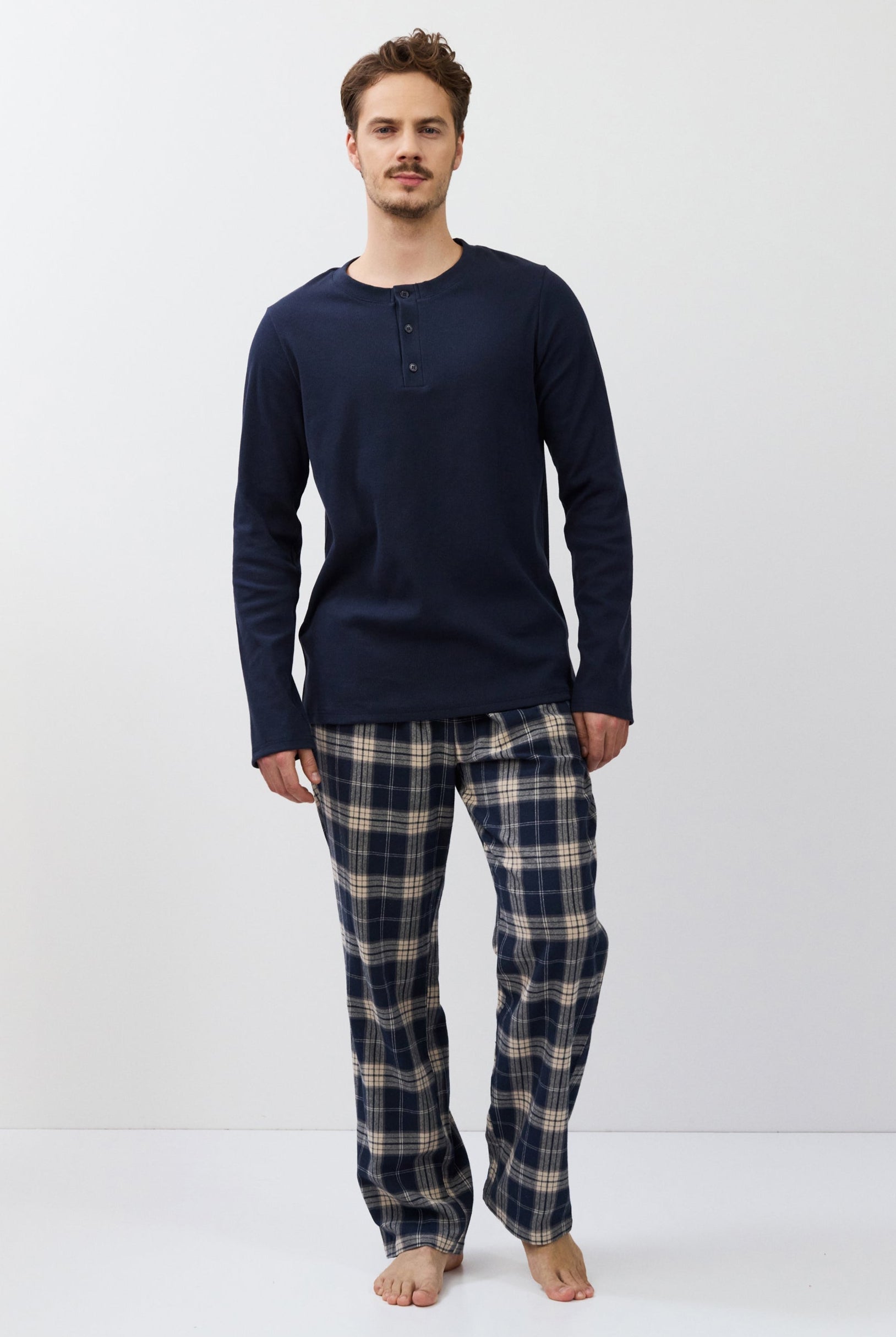 Man wearing a navy long-sleeve shirt and plaid pants on a white background
