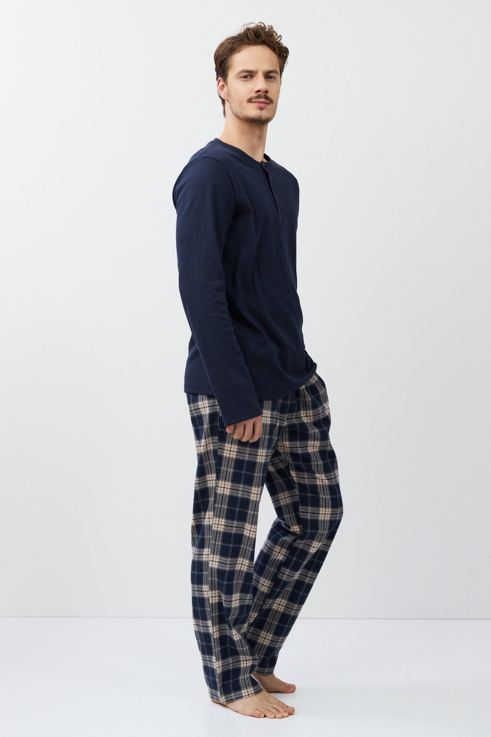 Man wearing navy long-sleeve top and plaid pants on a white background
