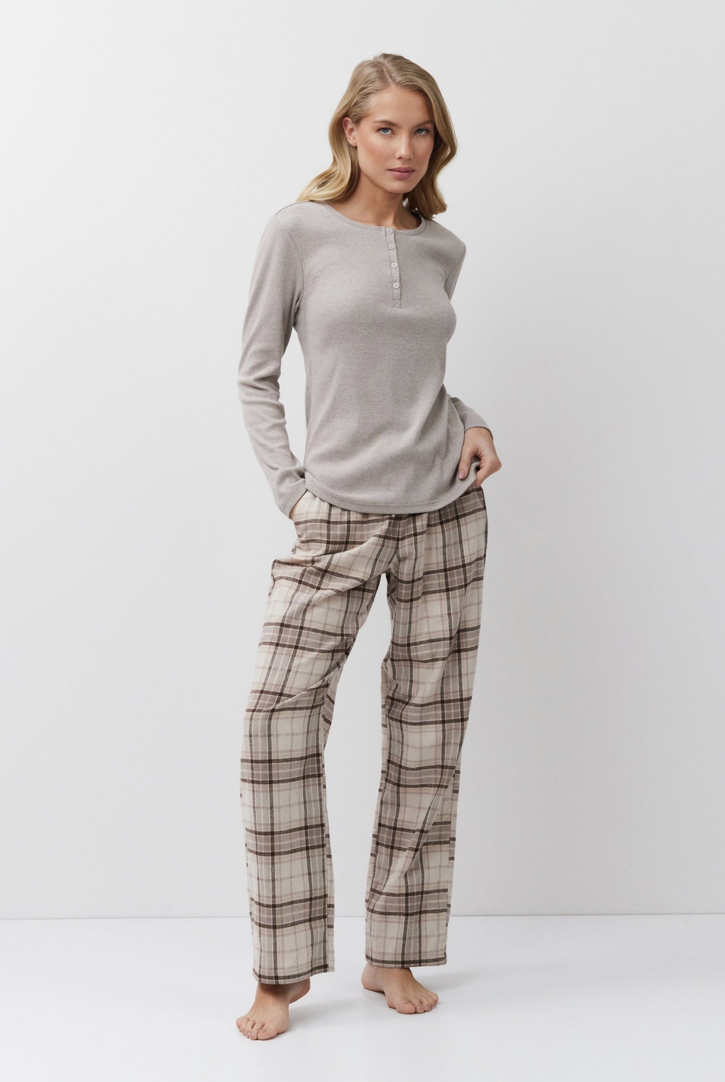 Woman wearing a beige long-sleeve top and plaid pants on a white background