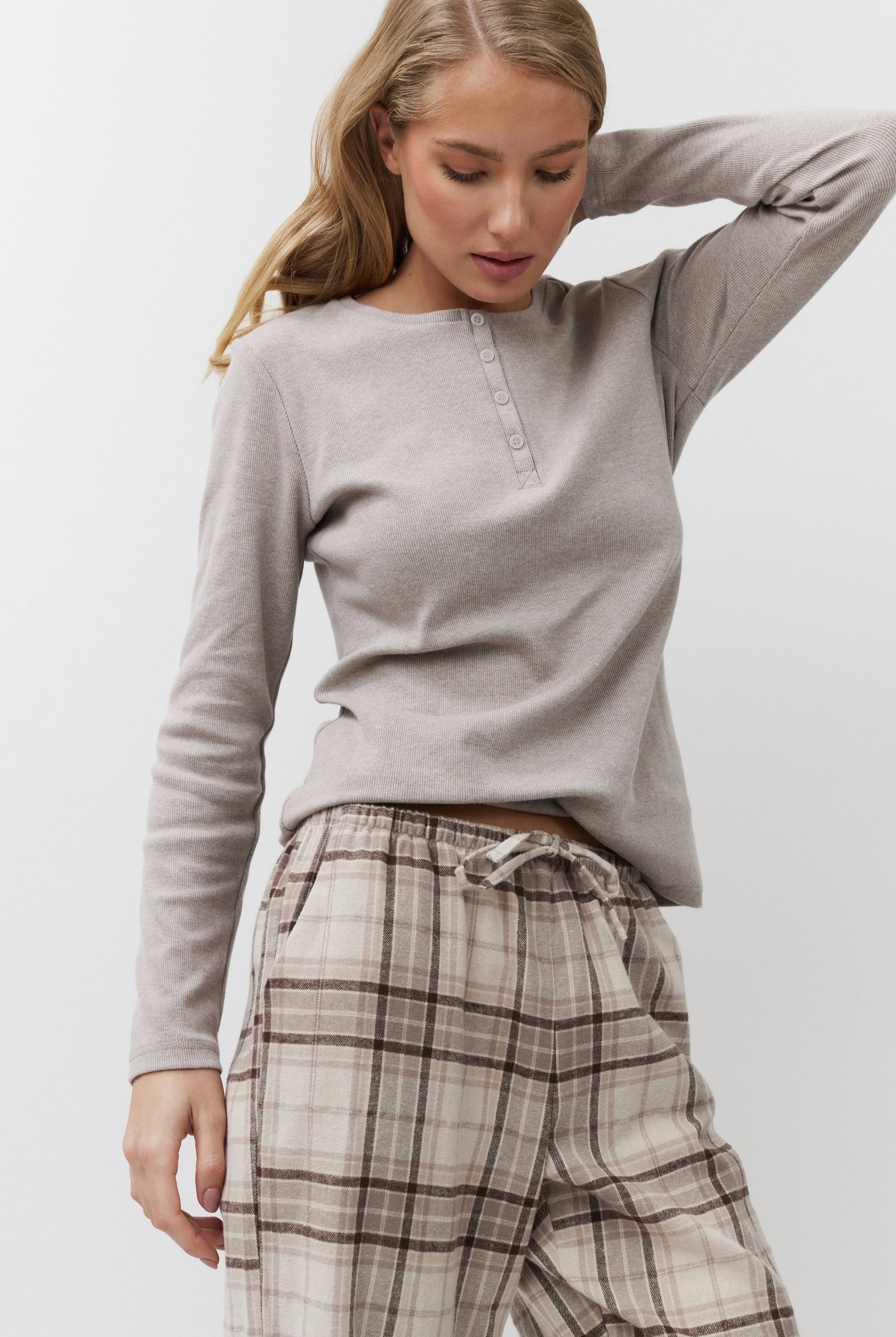 Woman wearing a beige long-sleeve top and plaid pants on a white background
