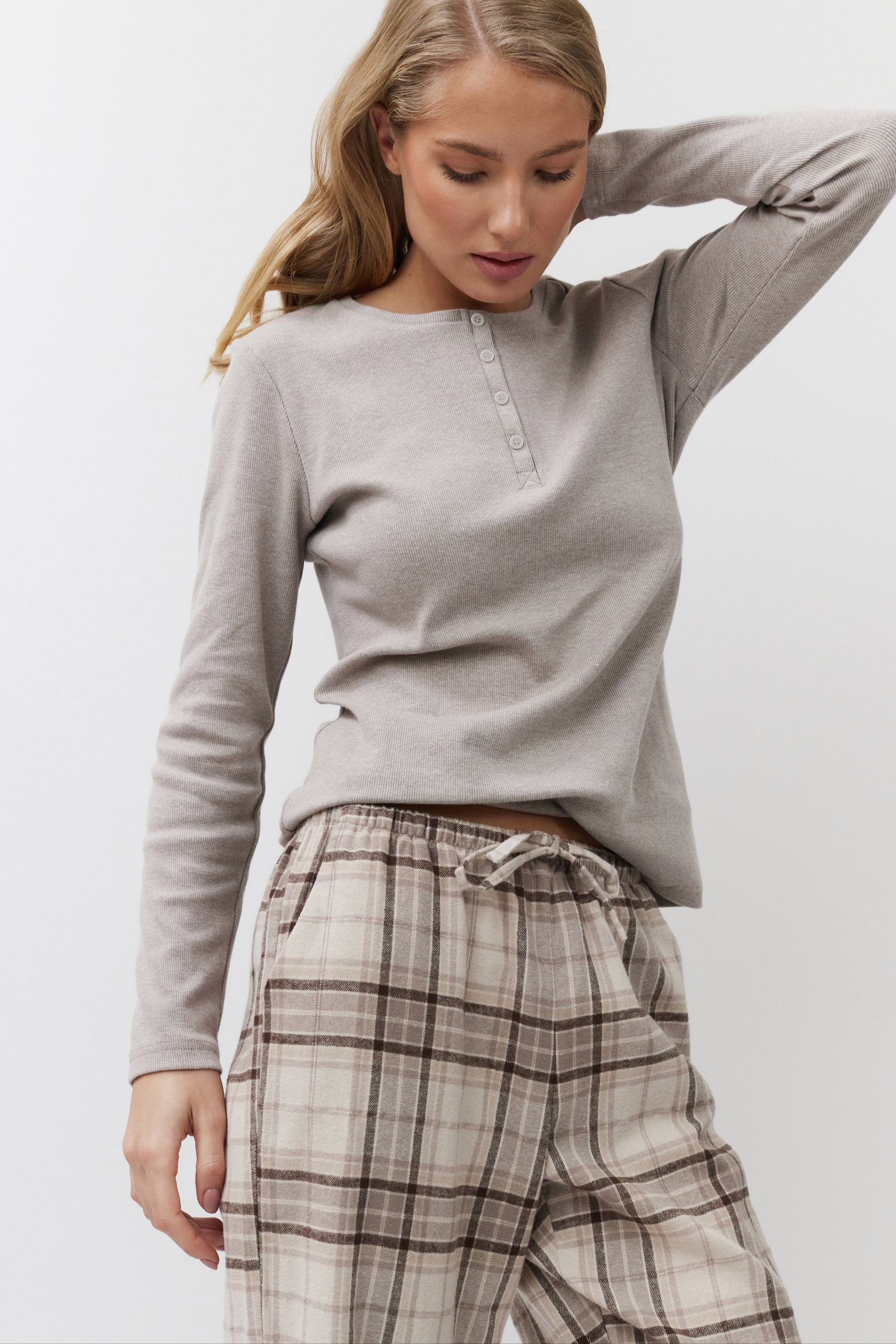 Woman wearing a beige long-sleeve top and plaid pants on a white background