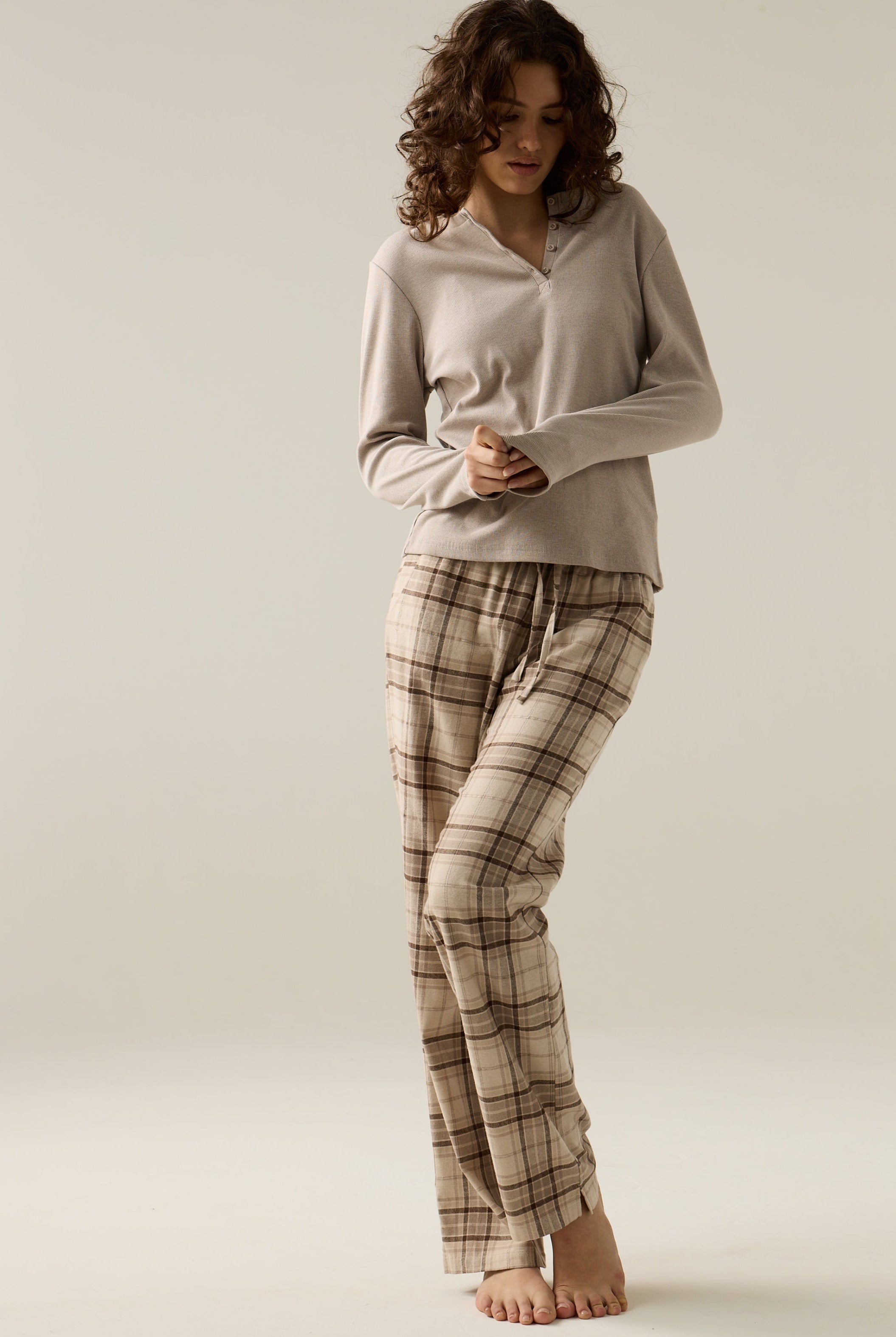 Woman wearing a beige top and plaid pants on a plain background