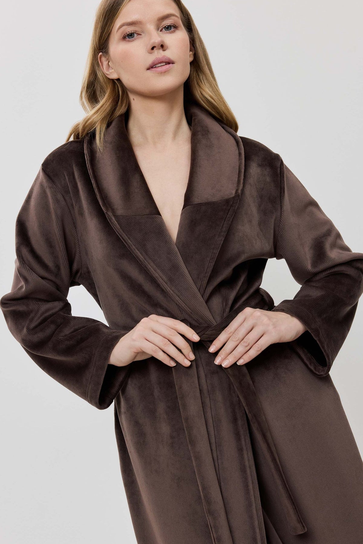 A woman wearing a long brown plush bathrobe with a tie belt.
