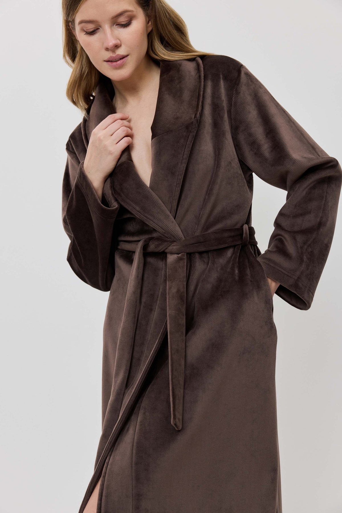 A woman wearing a long brown plush bathrobe with a tie belt.