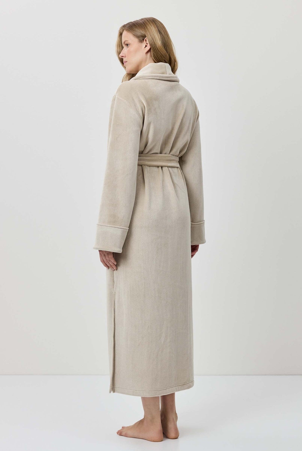 Woman wearing a beige robe standing against a white background