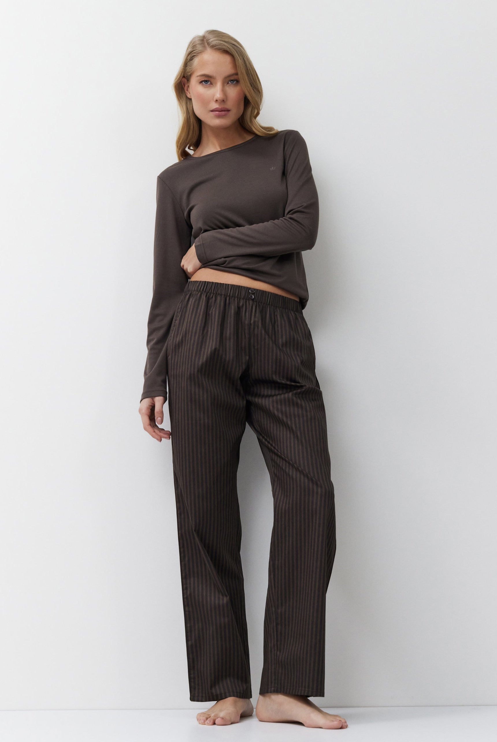 Woman wearing a brown outfit with a long-sleeve top and striped pants on a white background