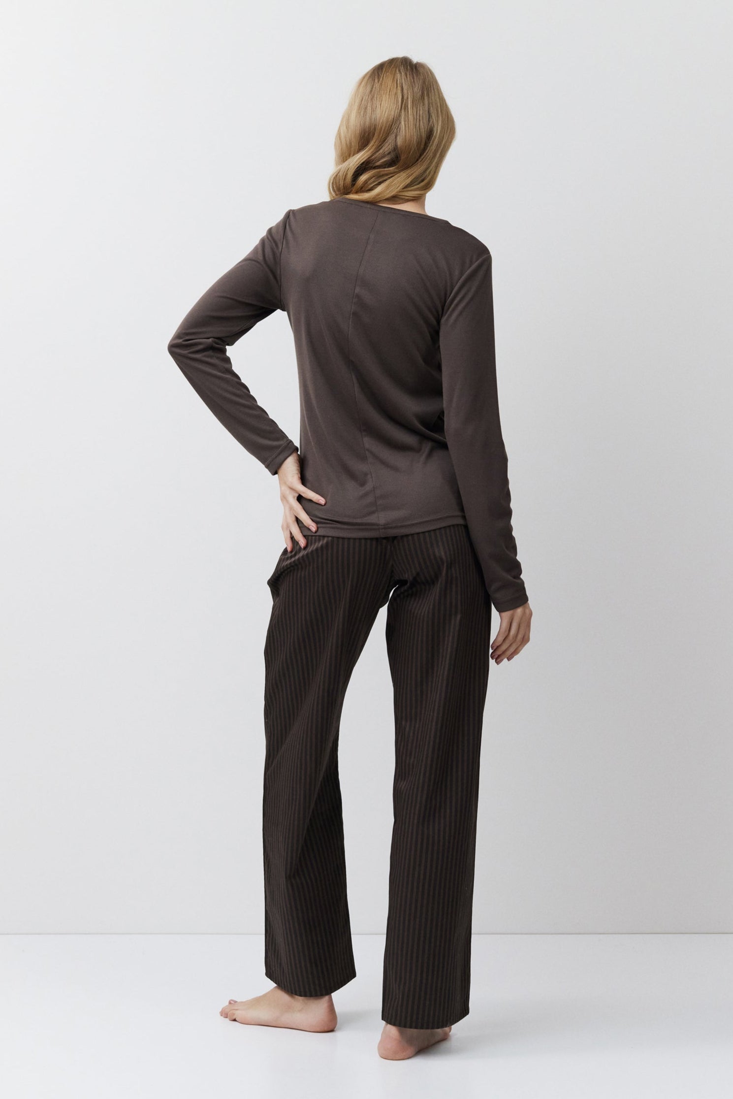 Person wearing a brown long-sleeve top and pants on a white background