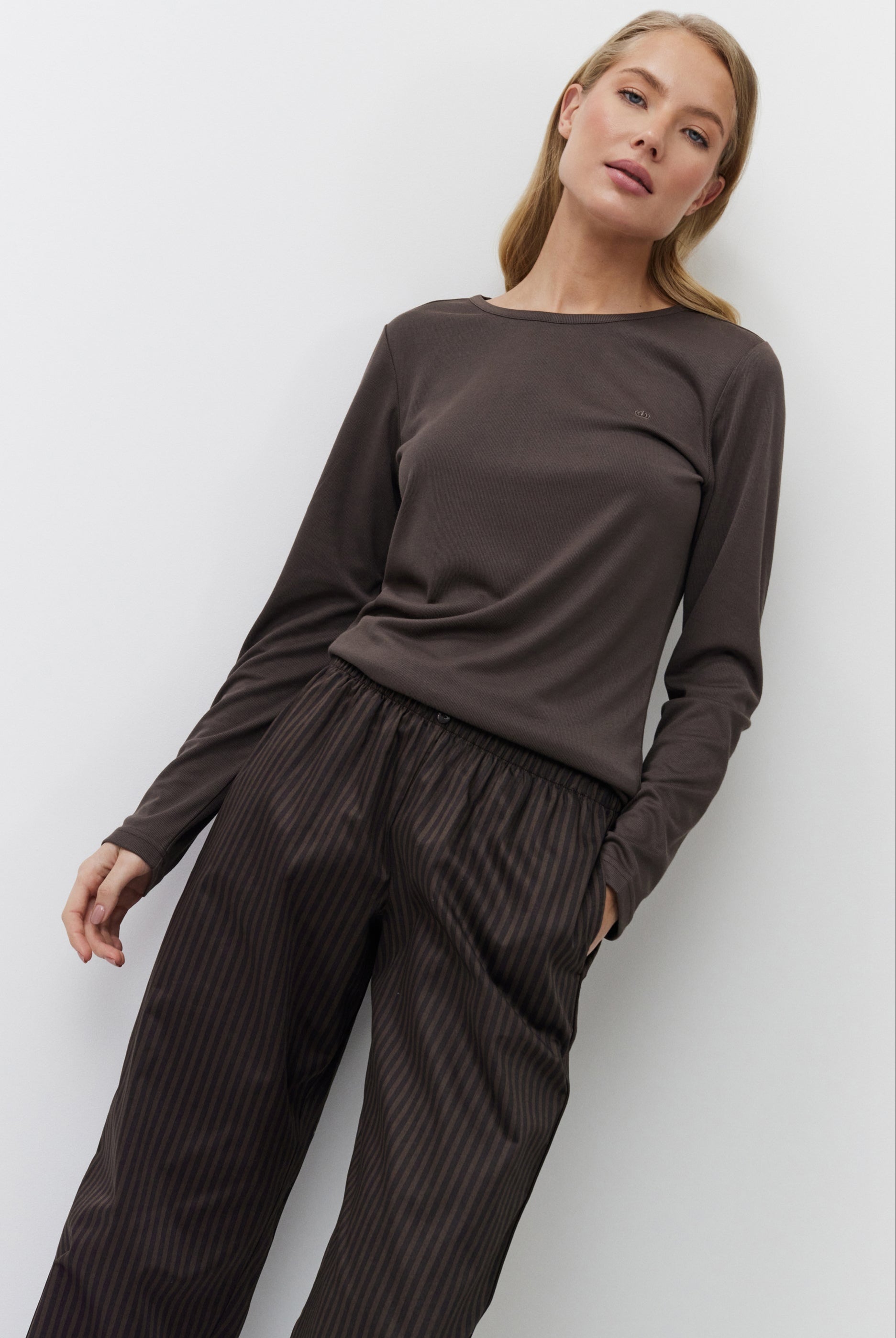 Woman wearing a brown long-sleeve top and dark pants against a white background