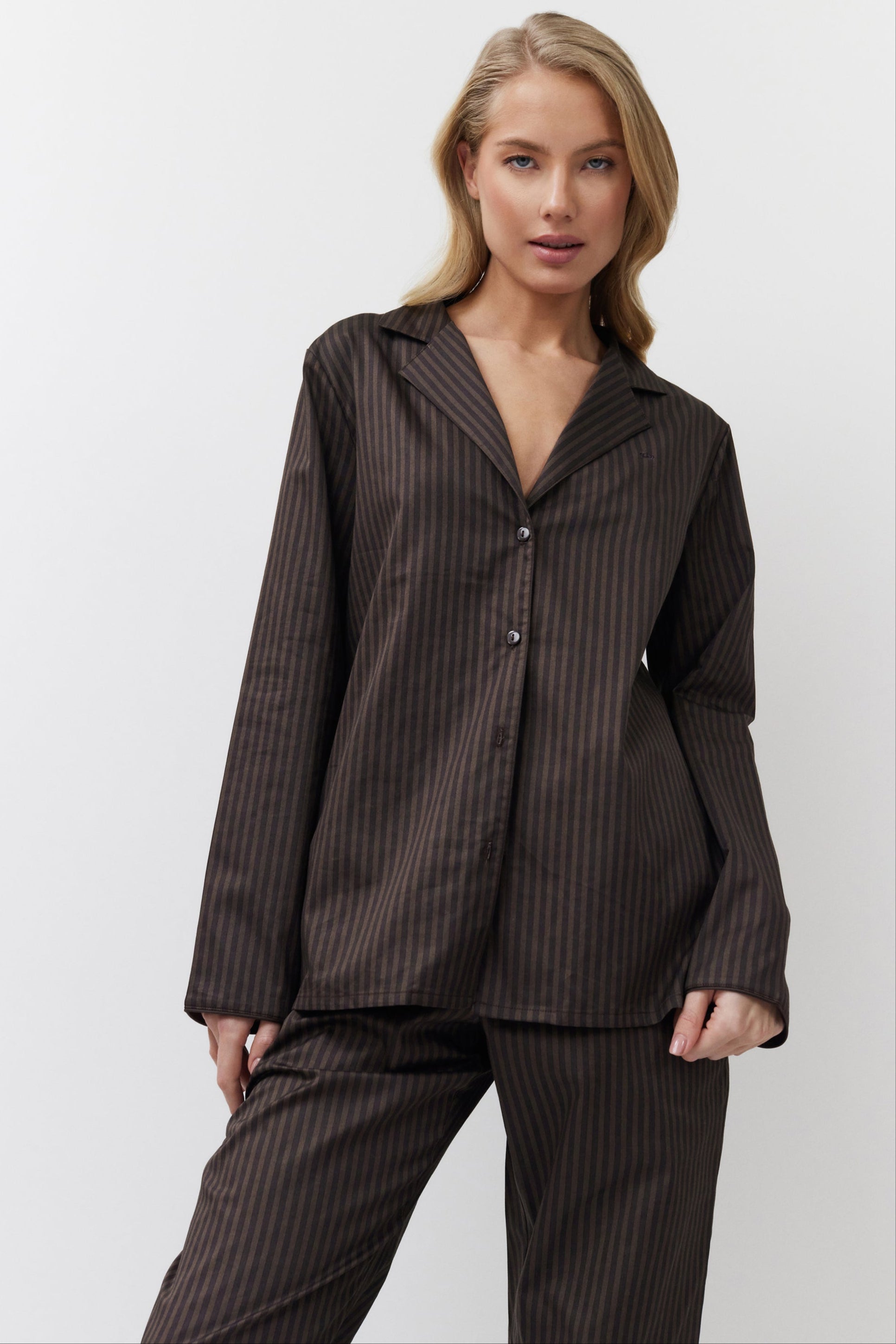Woman wearing a brown pinstripe pajama set against a white background
