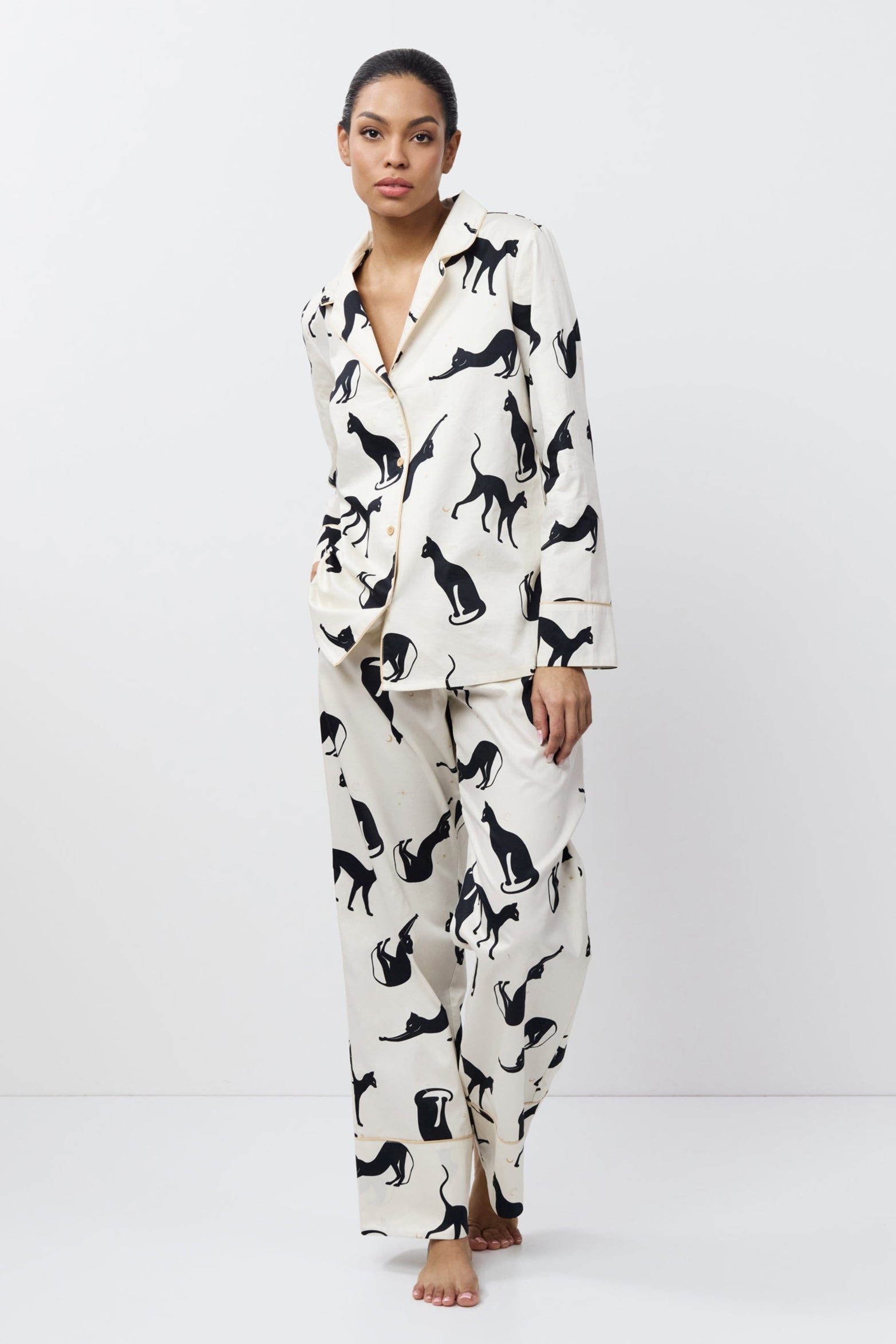 Woman wearing a white pajama set with black cat prints on a white background