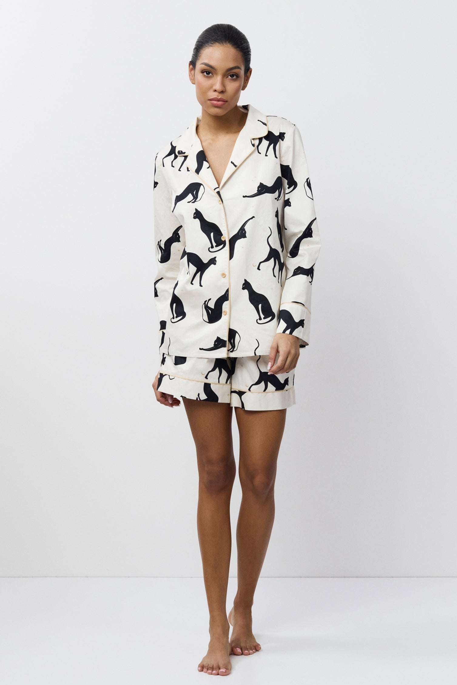 Person wearing a white pajama set with black cat prints on a white background