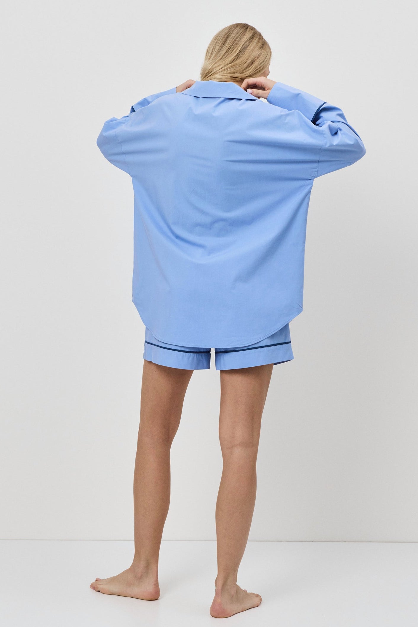 Person wearing a light blue oversized shirt and shorts set on a white background