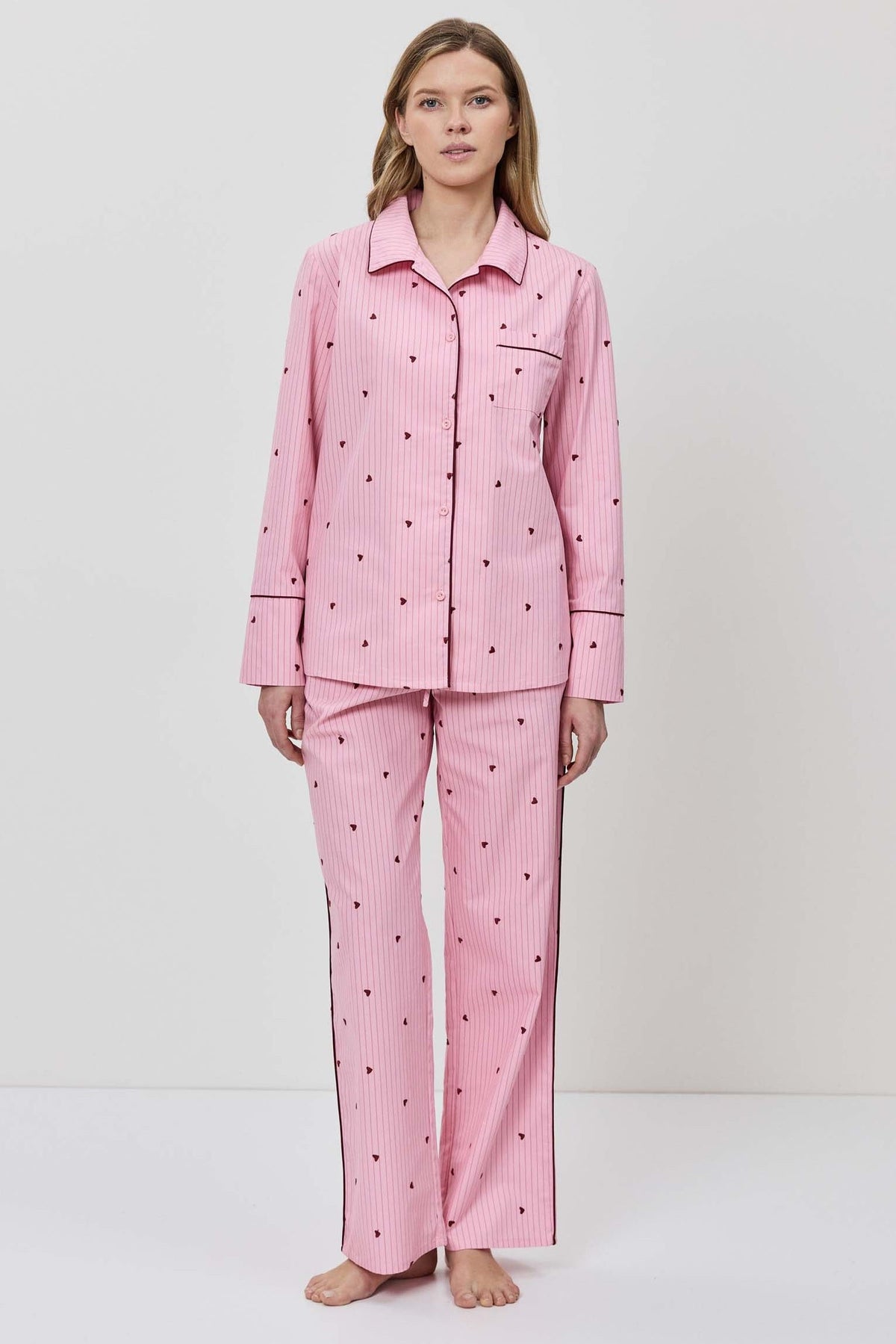 Person wearing a pink pajama set with hearts on a white background