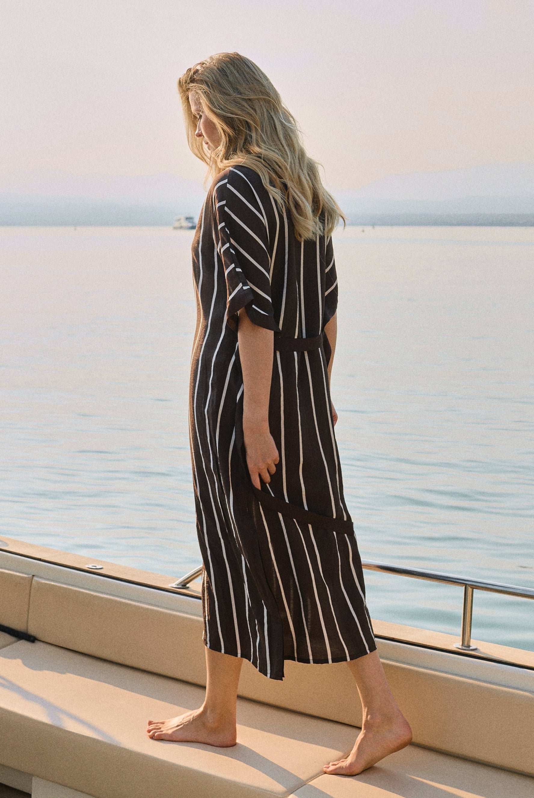 Woman in a striped dress standing on a boat deck with a scenic ocean view.