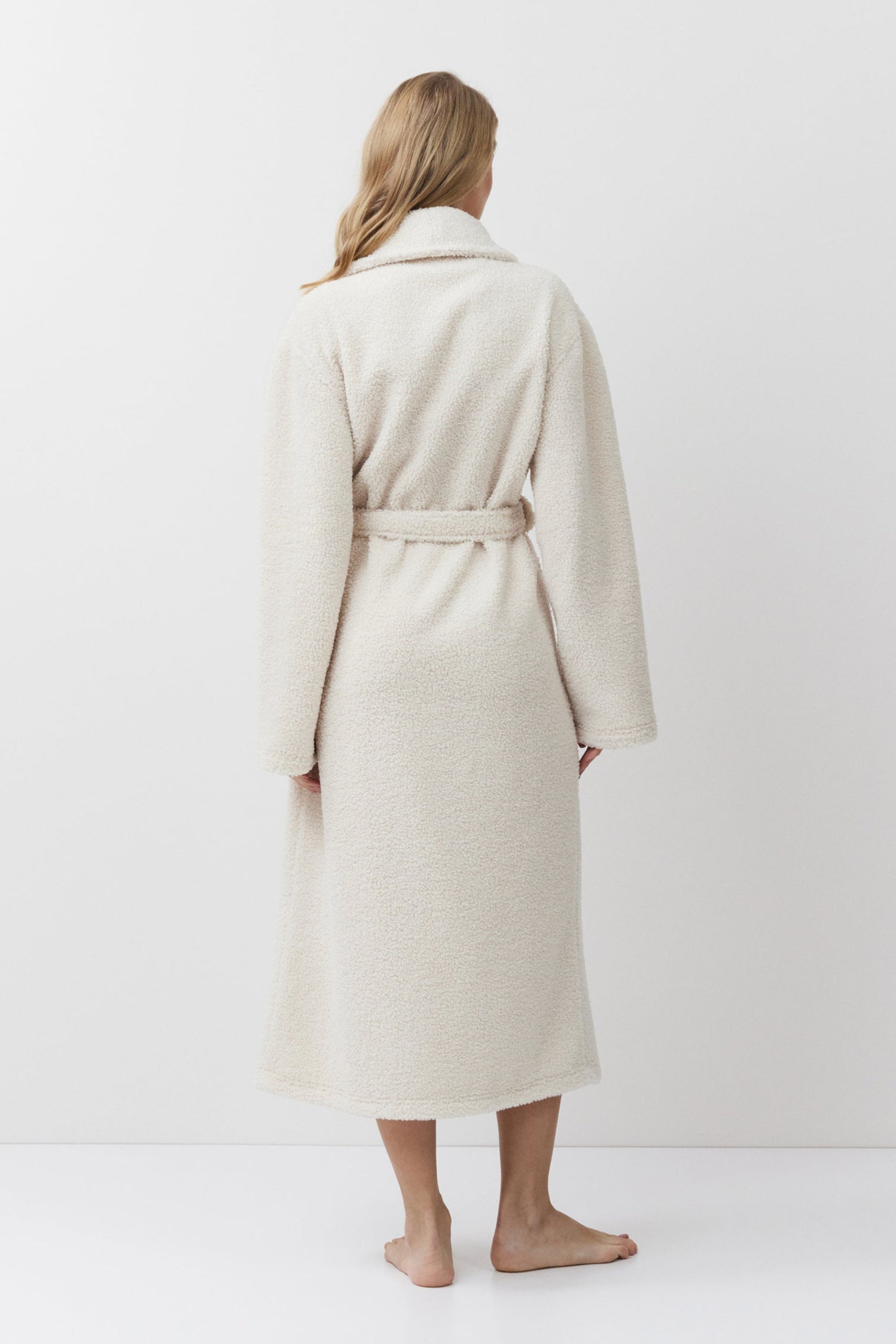 Person wearing a beige bathrobe standing against a white background