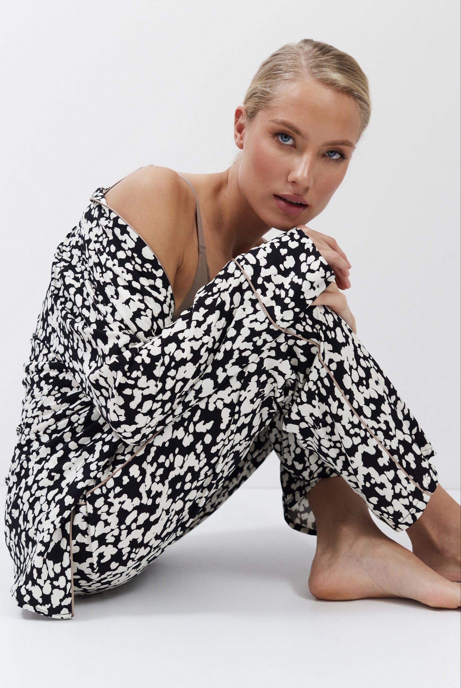 Woman wearing a black and white patterned pajama set sitting on a white background