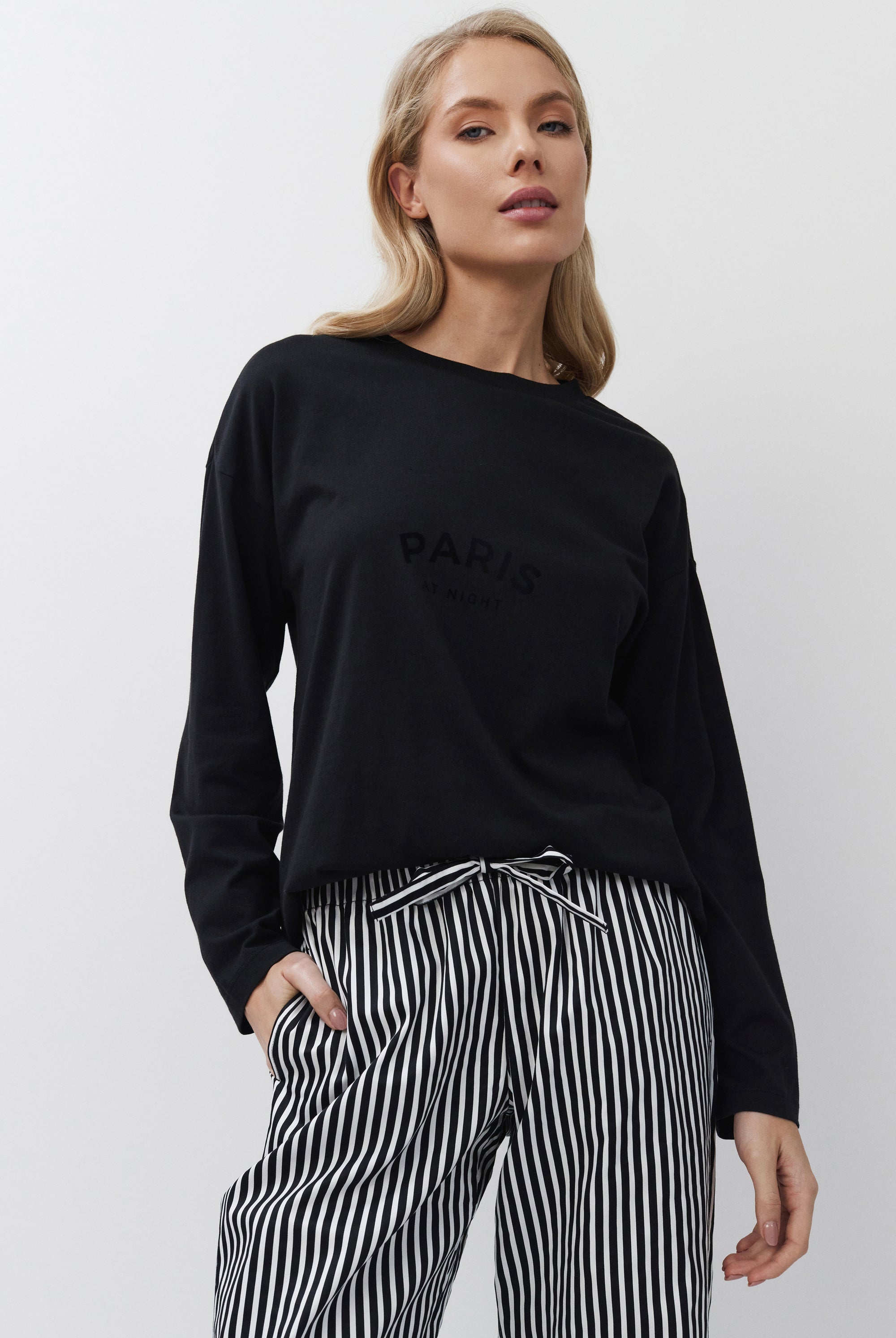 Woman wearing a black sweatshirt with 'Paris' text and striped pants on a white background
