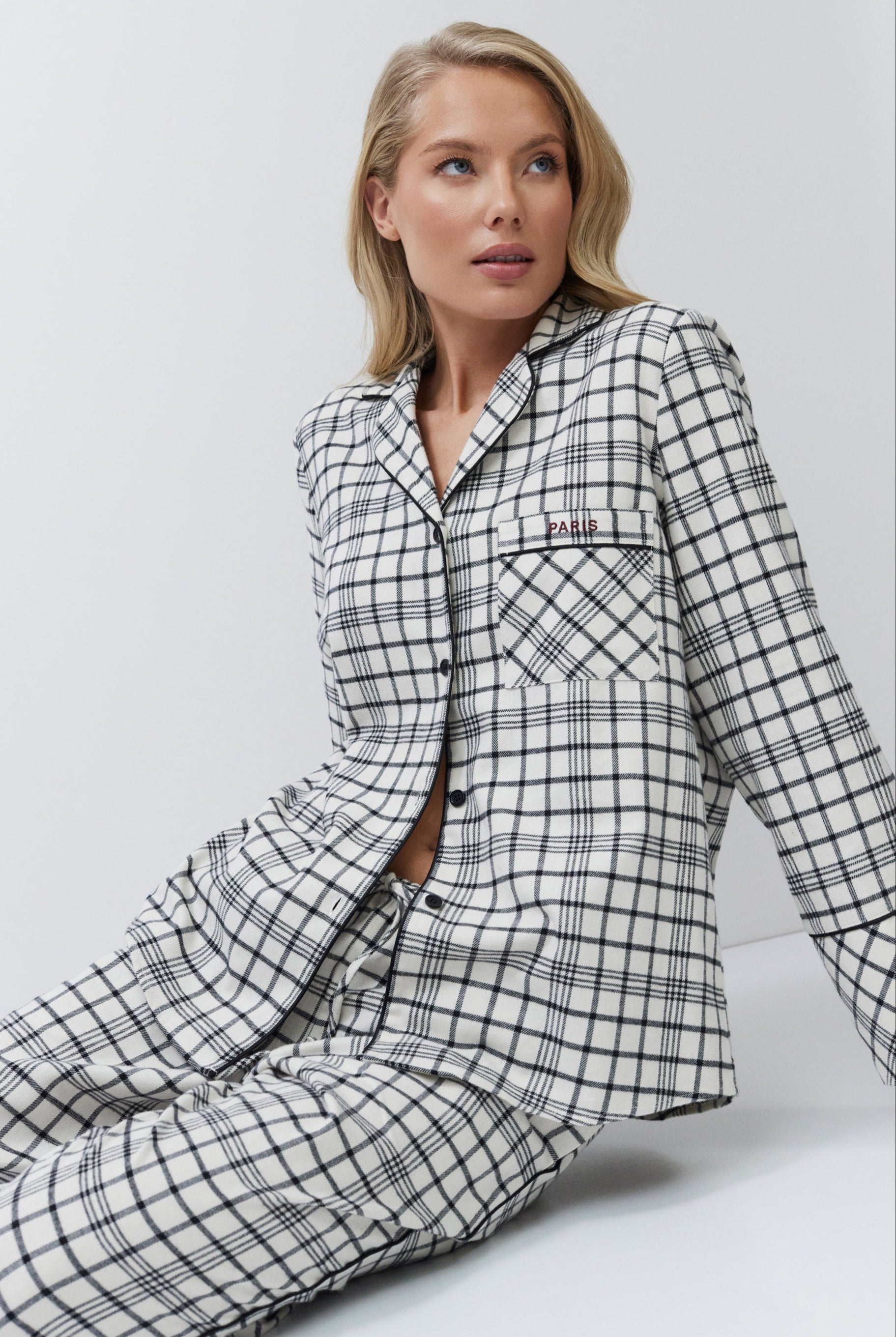 Woman wearing a black and white checkered pajama set sitting on a white background