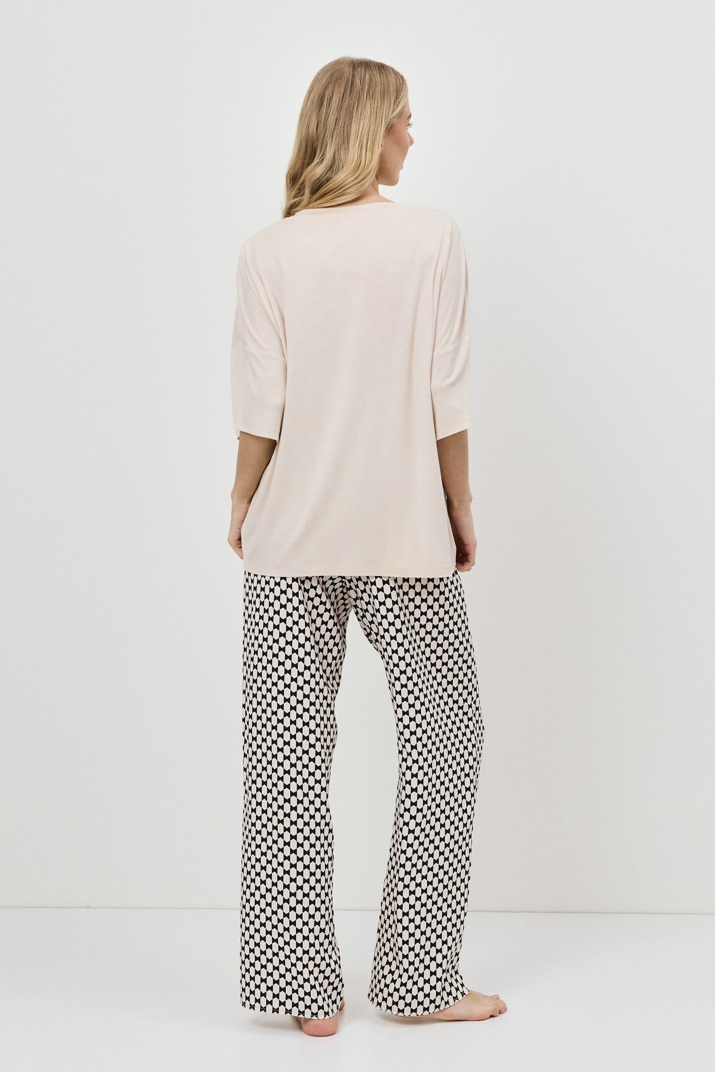 Woman wearing a beige top and patterned pajama pants on a white background