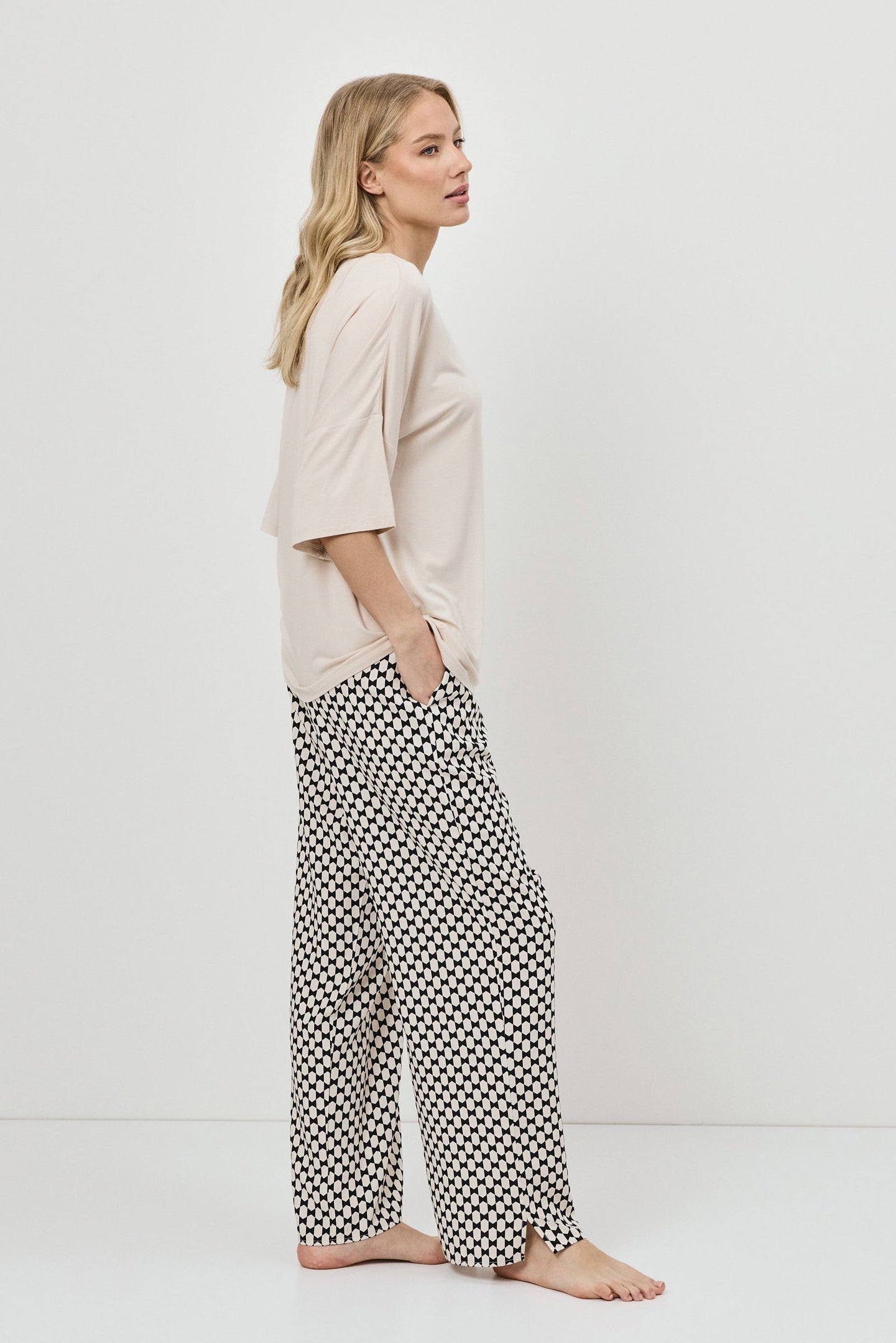 Woman wearing a beige top and patterned pants against a white background
