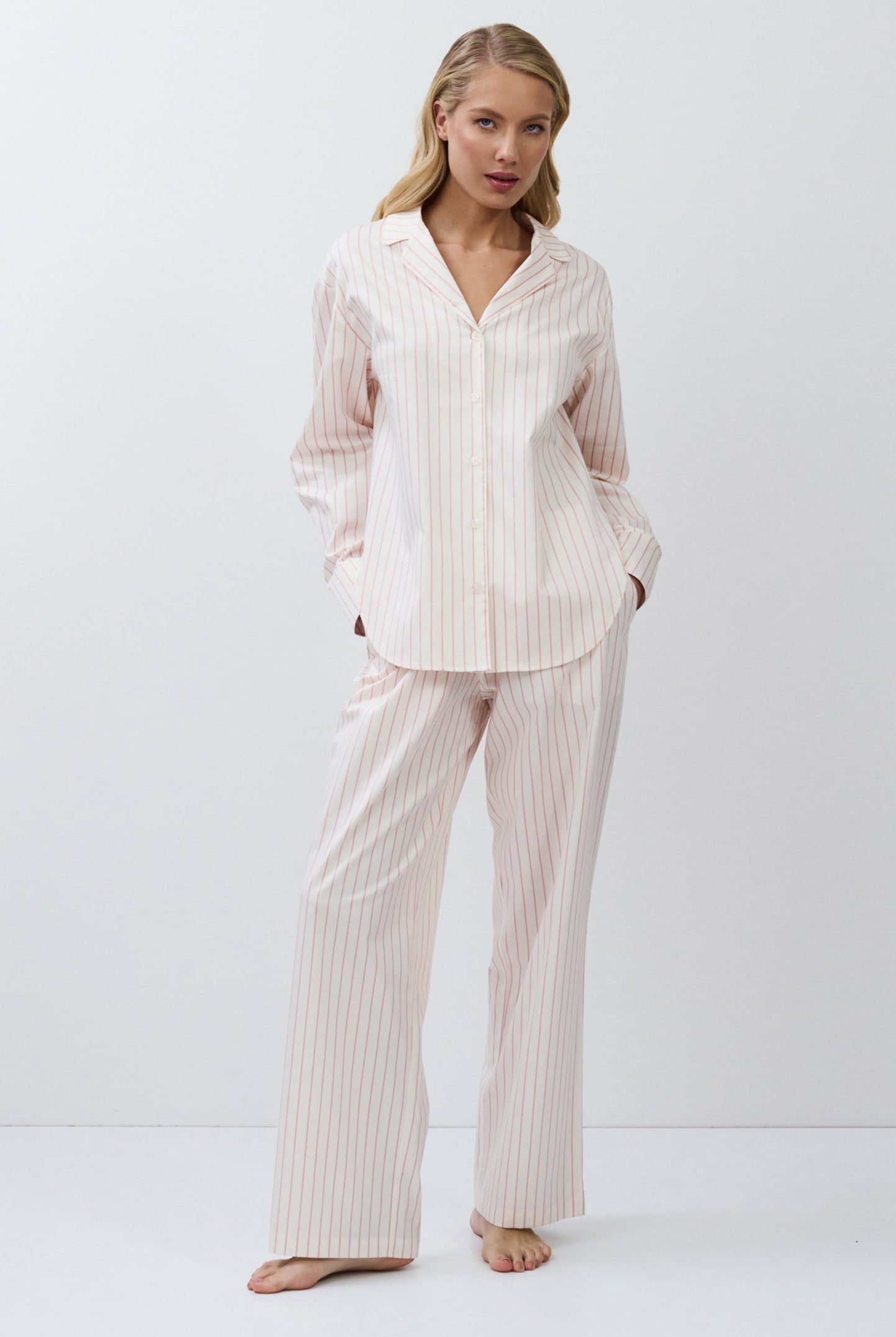 Woman wearing a light pink striped pajama set on a white background