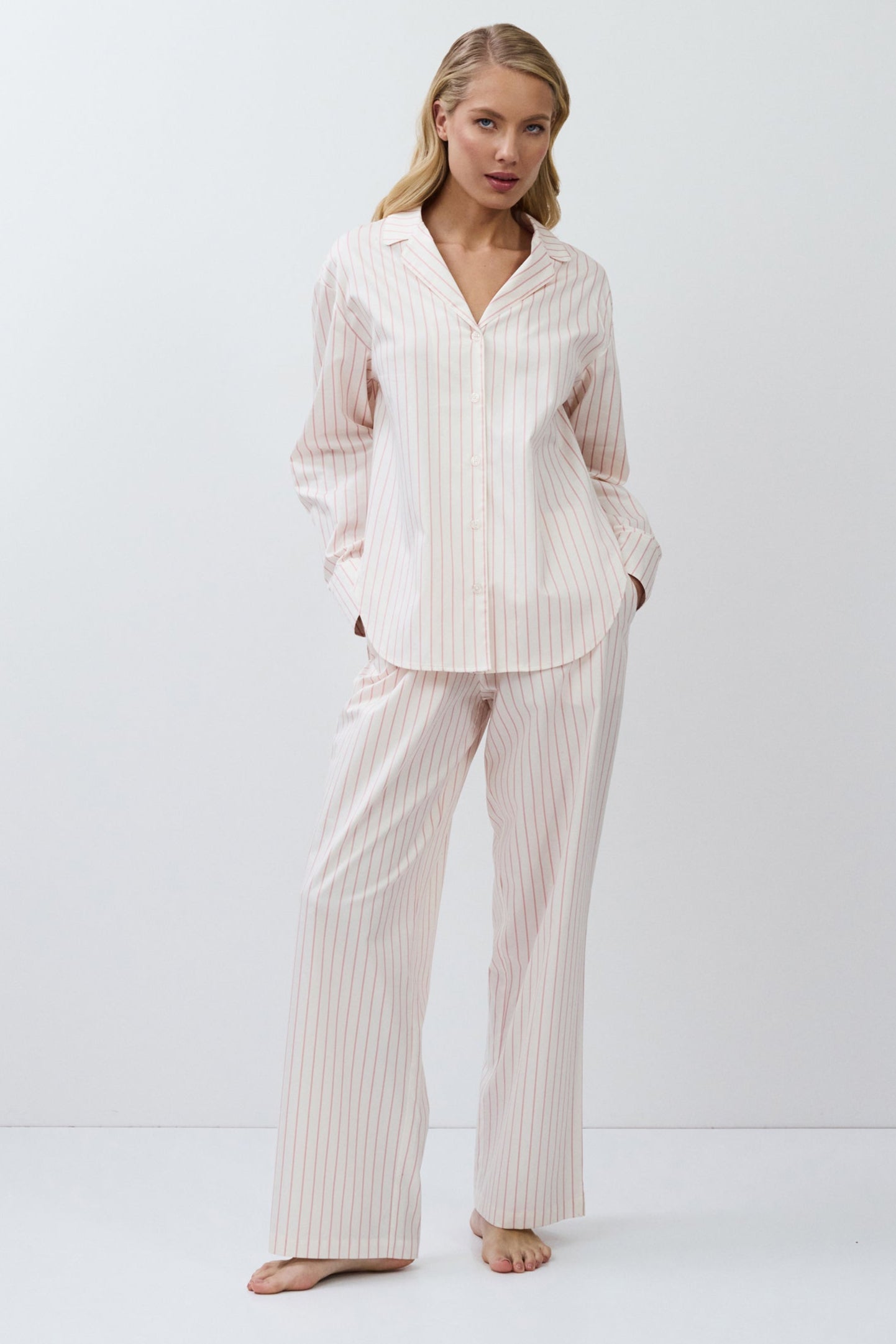 Woman wearing a light pink striped pajama set on a white background